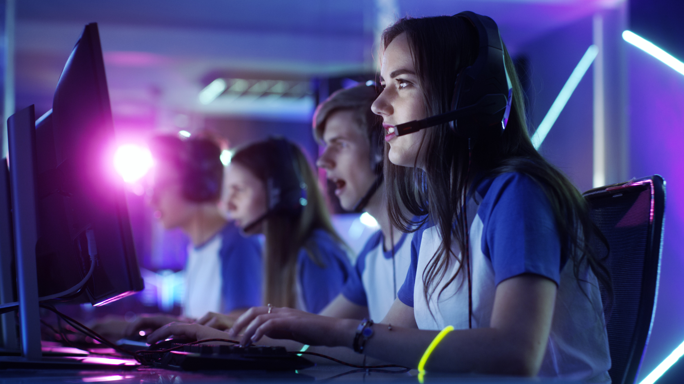 A young woman wearing a headset sits beside her teammates while competing in an esports competition on a computer.