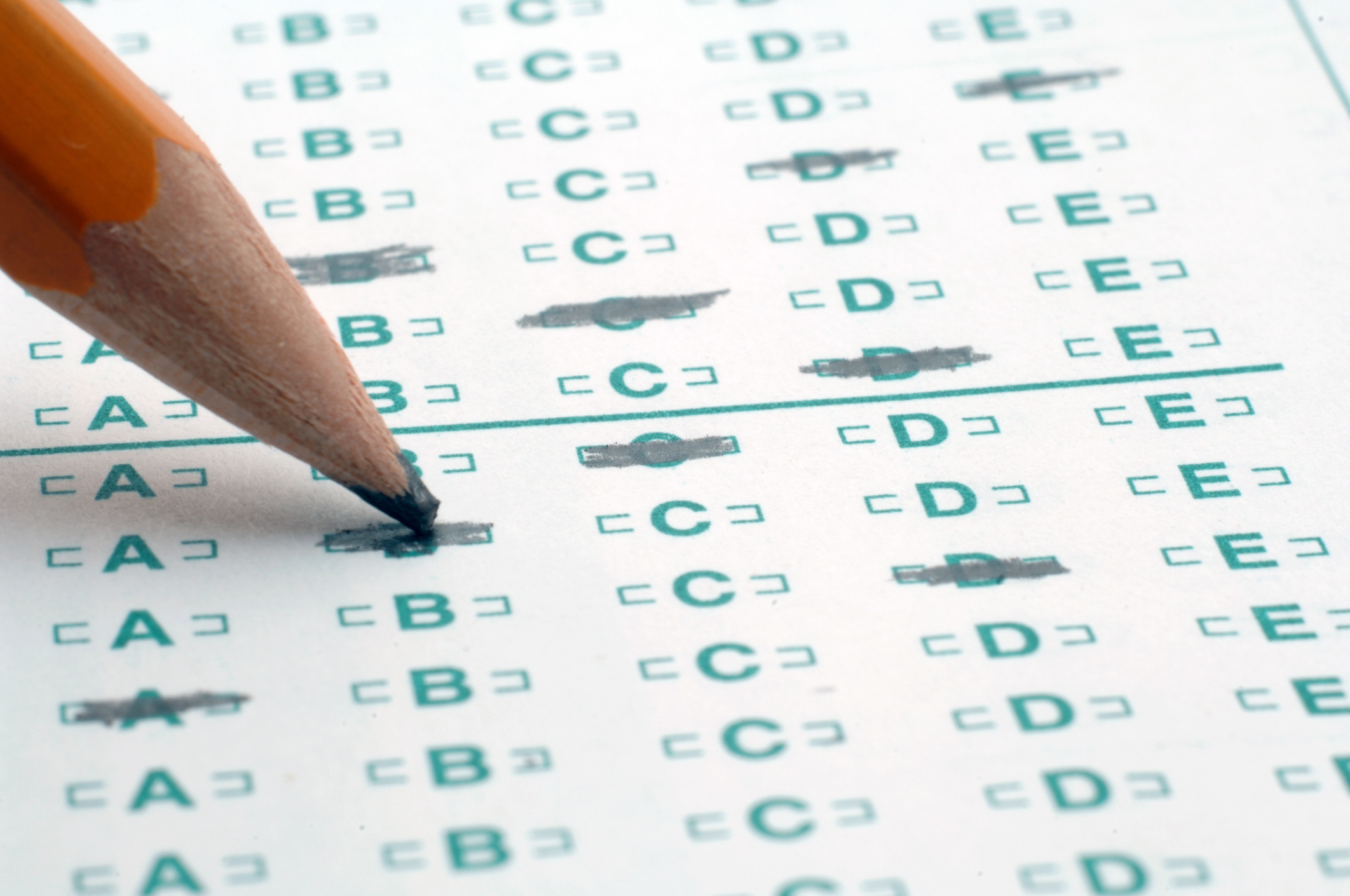 A close-up of a pencil bubbling in an answer on a green scantron sheet.