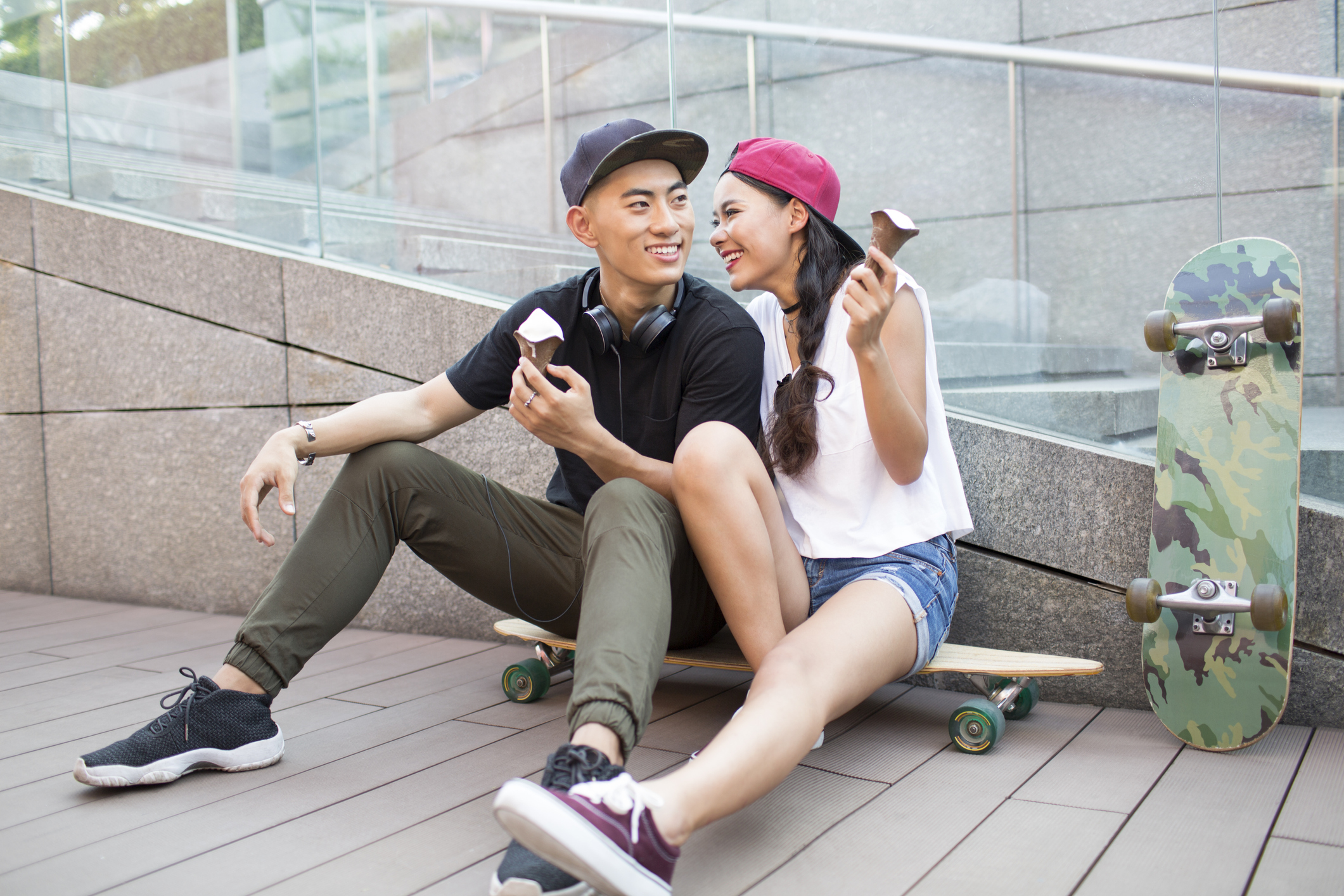Cheerful young couple eating ice cream on skateboard