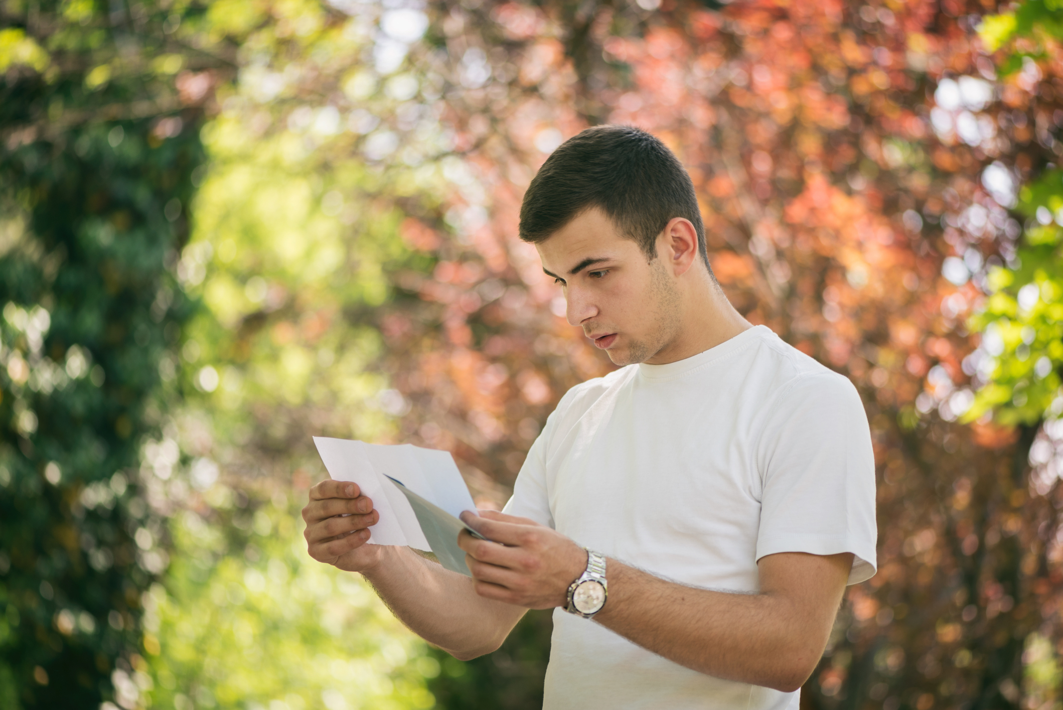 A young man looks surprised as he reads a letter outside.