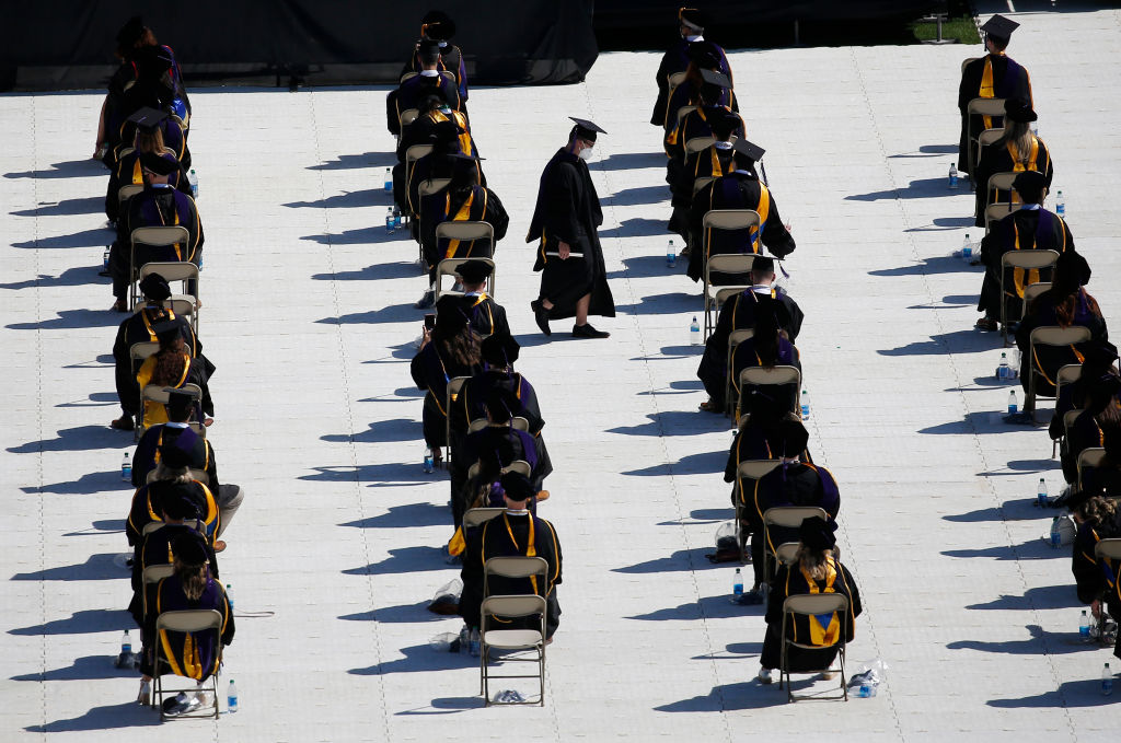 A graduate carries his diploma as he walks between rows of socially distanced colleagues