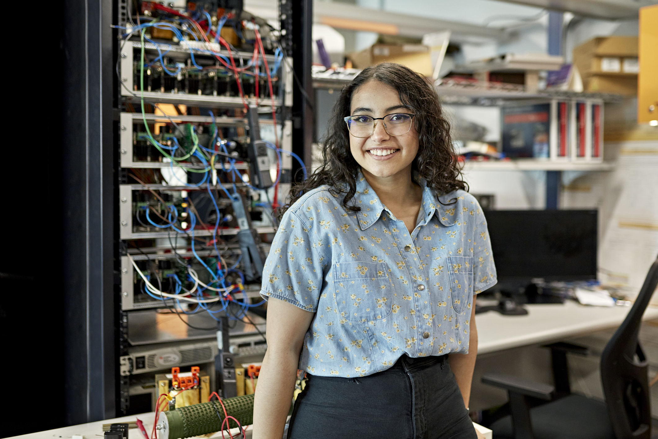 Latina electrical engineering college student standing in a tech lab and smiling at the camera.