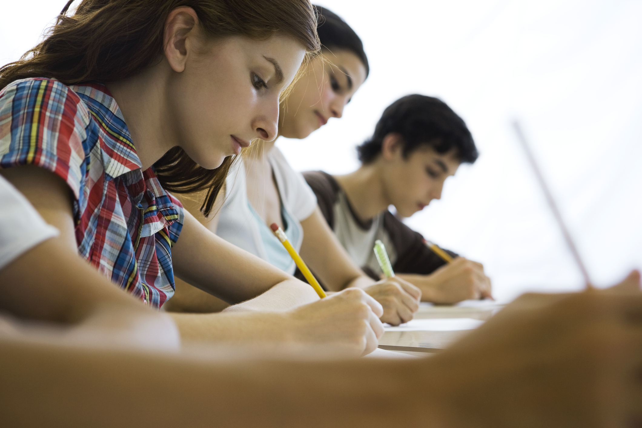 A group of high school students sitting at tables in a classroom. They are writing answers on a paper exam.