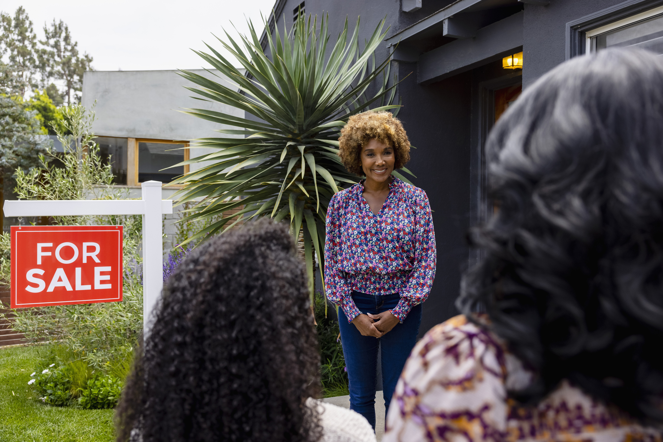 Smiling female real estate agent greeting customers outside house