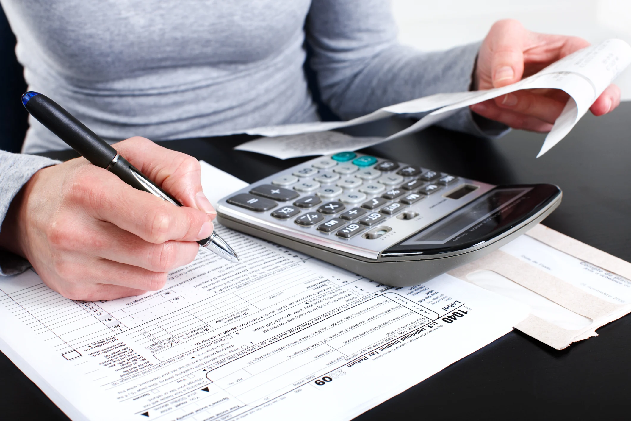 Close-up shot of a person using a calculator and a pen to work on their taxes.