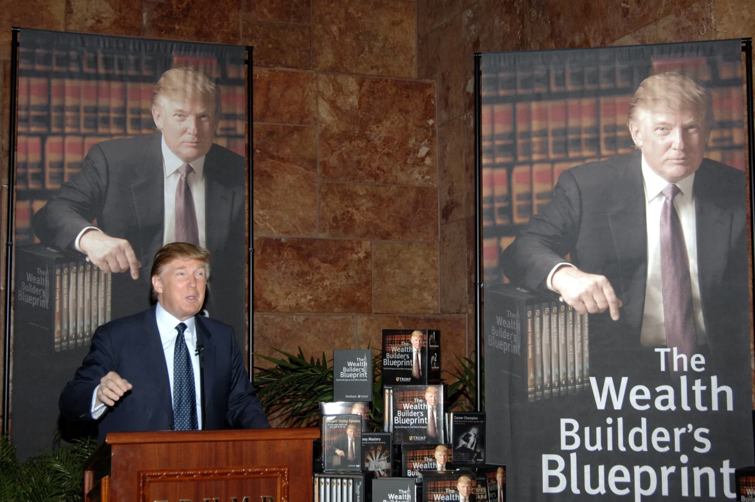 Donald Trump speaks at a podium on his book, The Wealth Builders Blue Print