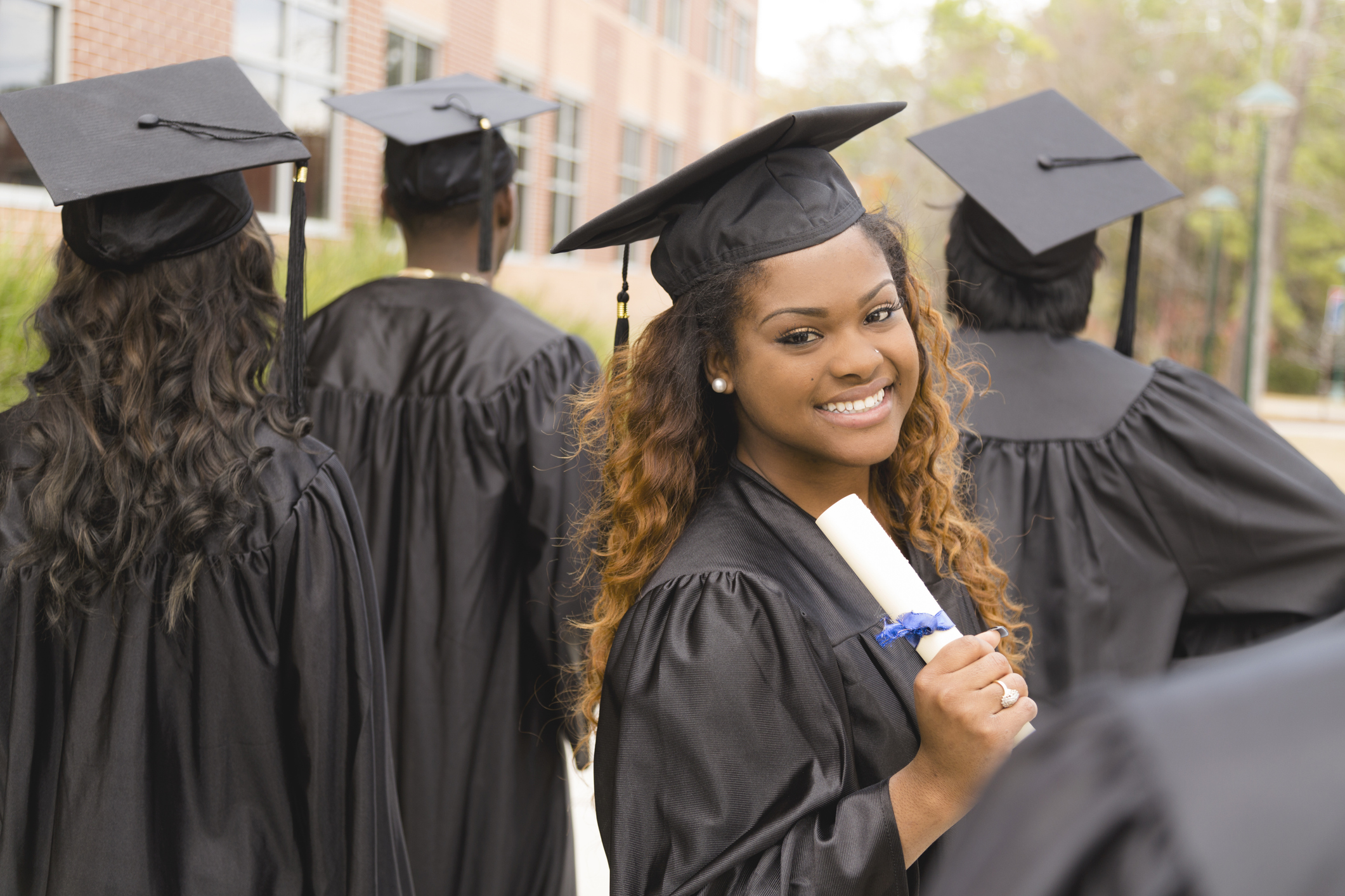 Excited Black female college graduate holding her diploma walks with classmates after the graduation ceremony.