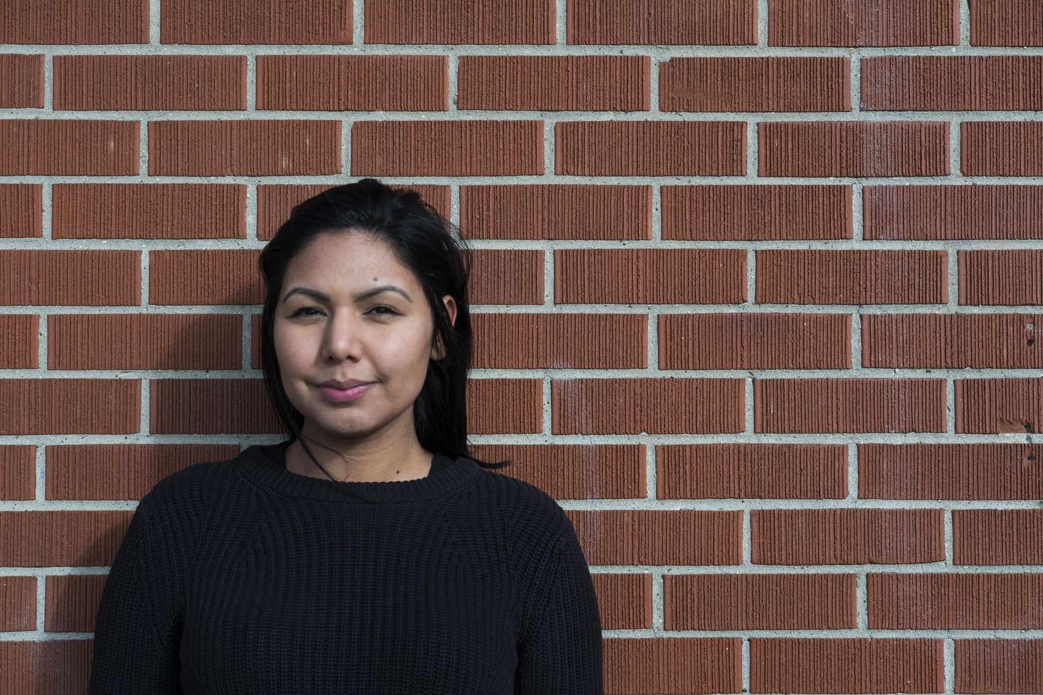 Indigenous college-aged woman standing against a brick wall.