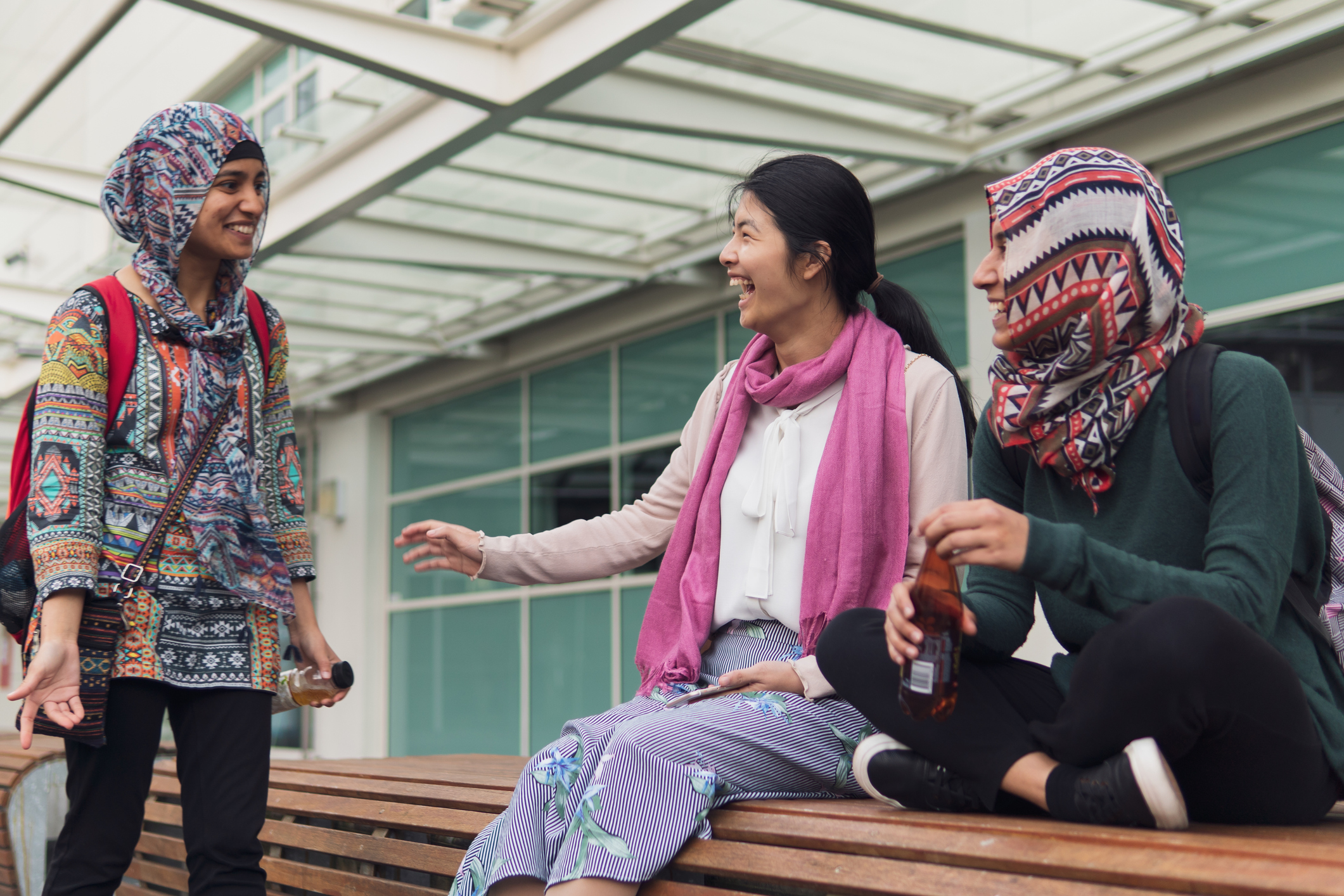 A group of female Muslim college students hanging out by a bench on their university's campus.