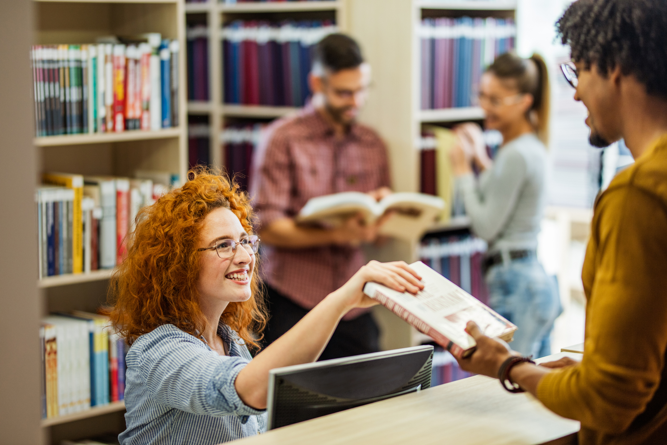 College library assistant sits at a desk checking a student's books back in.