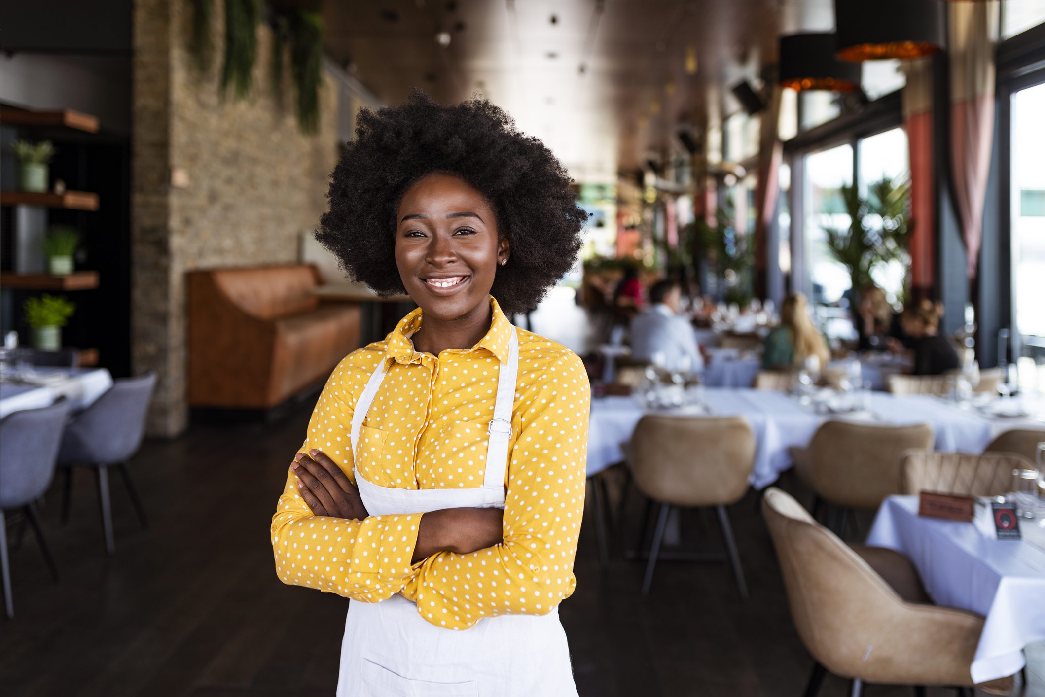 College-aged woman working in a coffee shop looks at the camera and smiles.