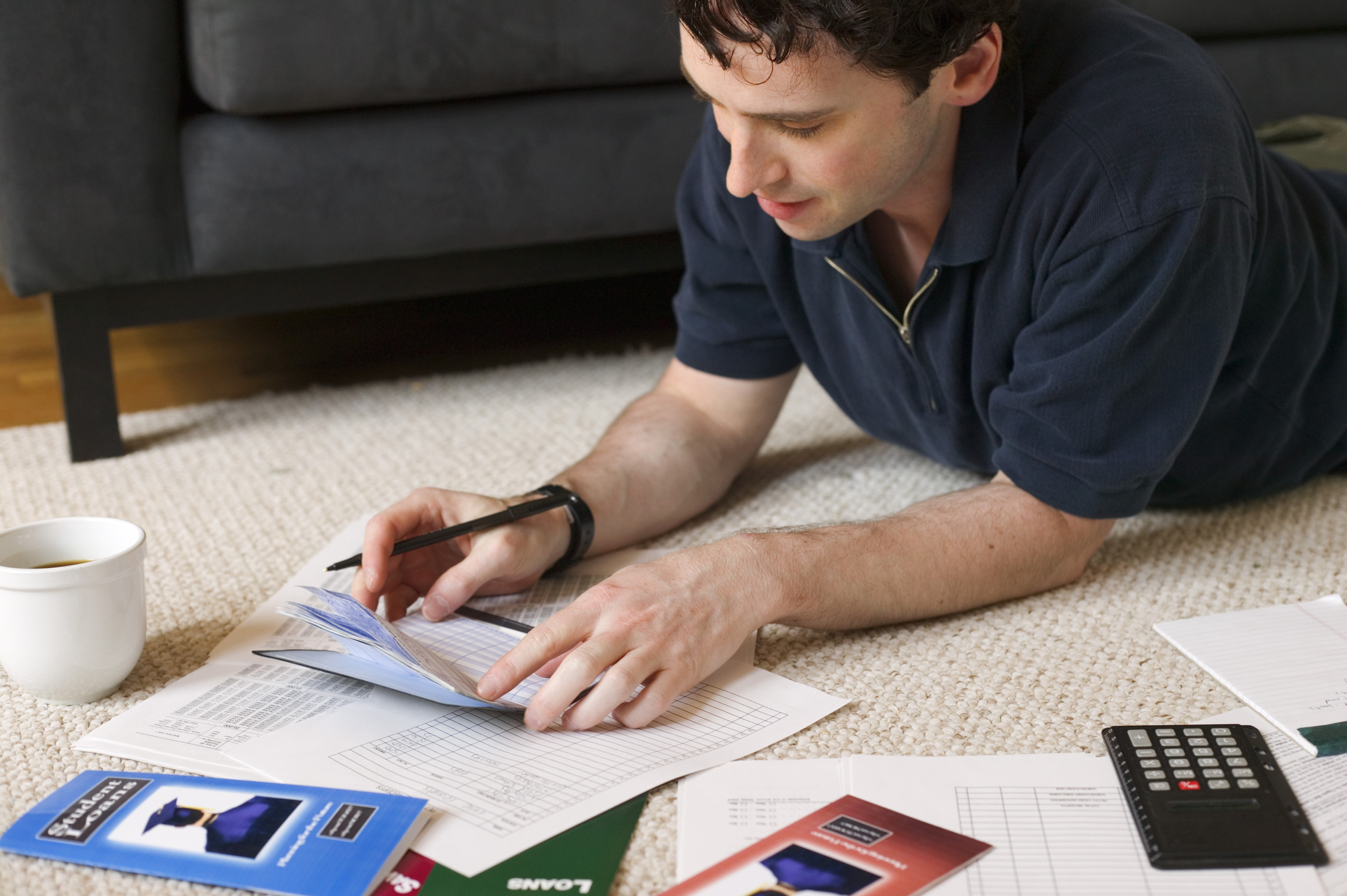 College graduate sitting in his living room paying bills.