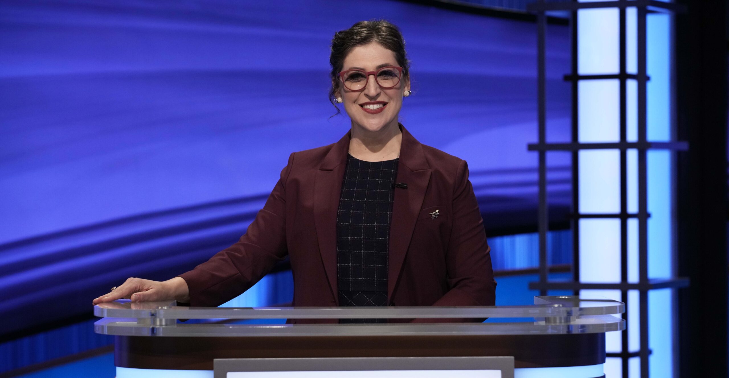 Jeopardy! host Mayim Bialik standing on set