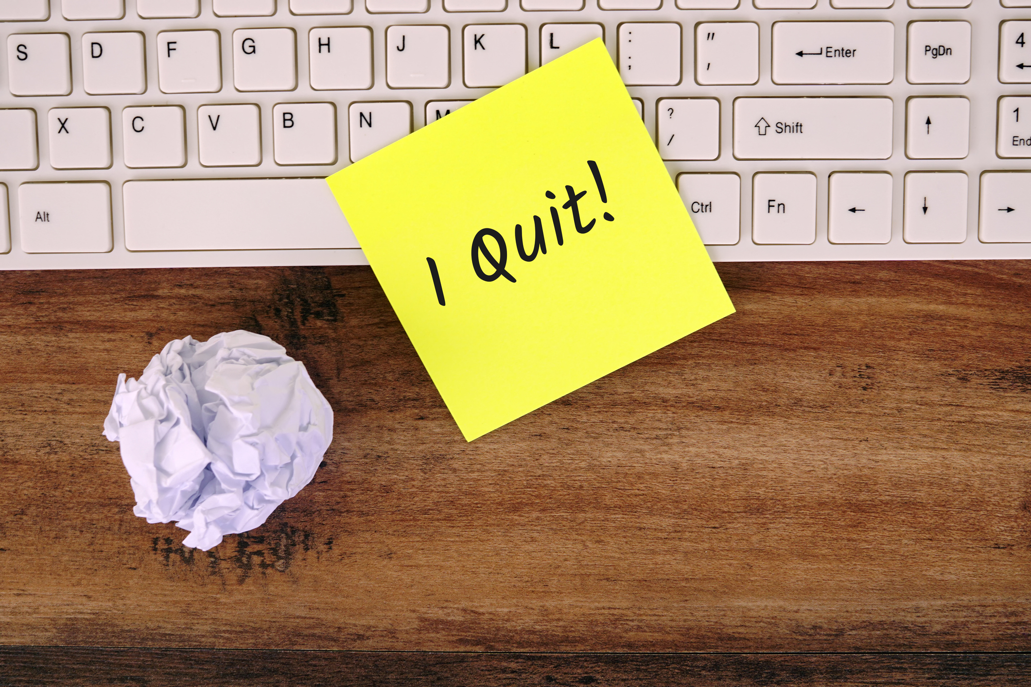 Post-it note with the words, "I Quite!" written on it is placed on top of a keyboard on a worker's office computer.