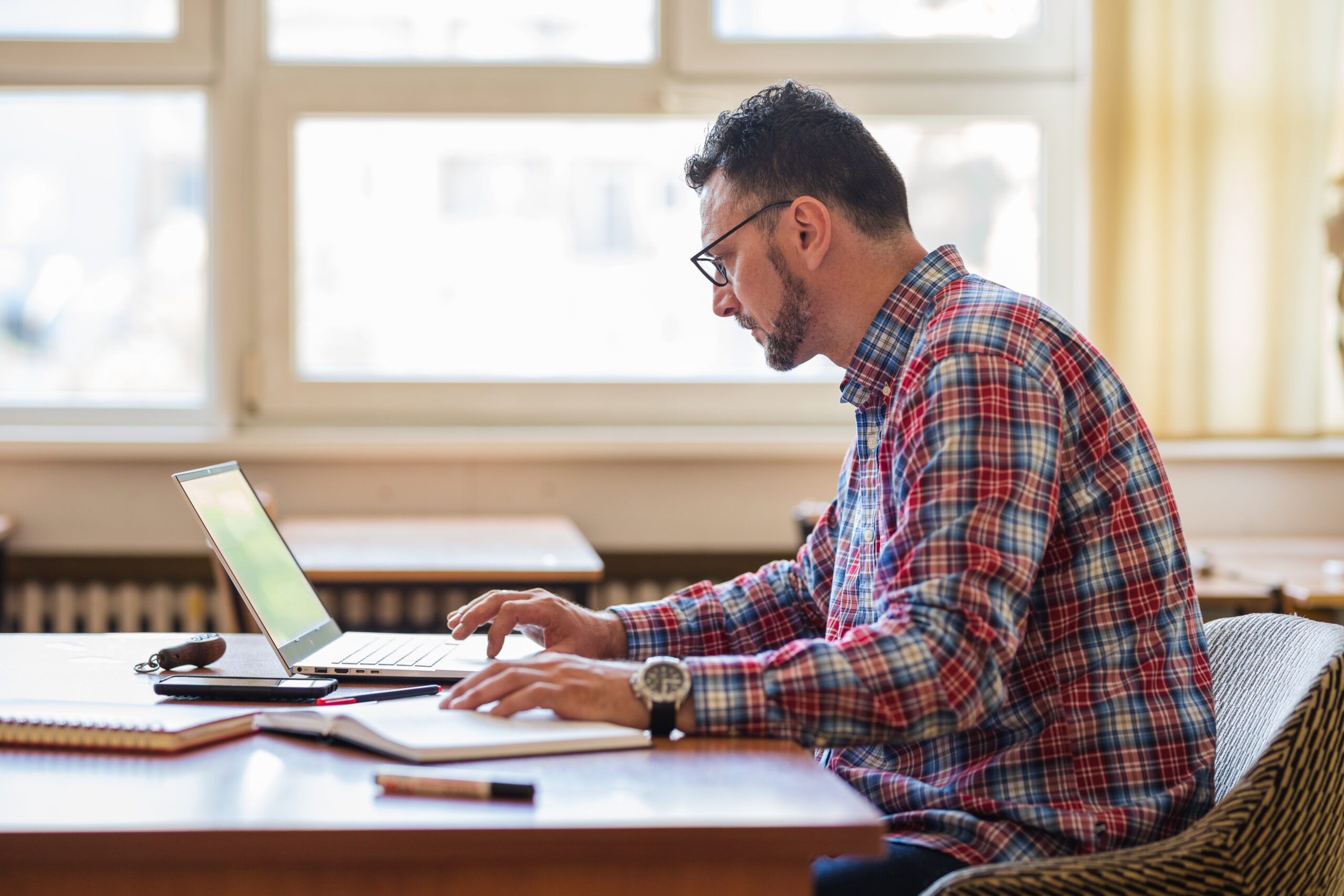 Man wearing eyeglasses while sitting in classroom and using laptop