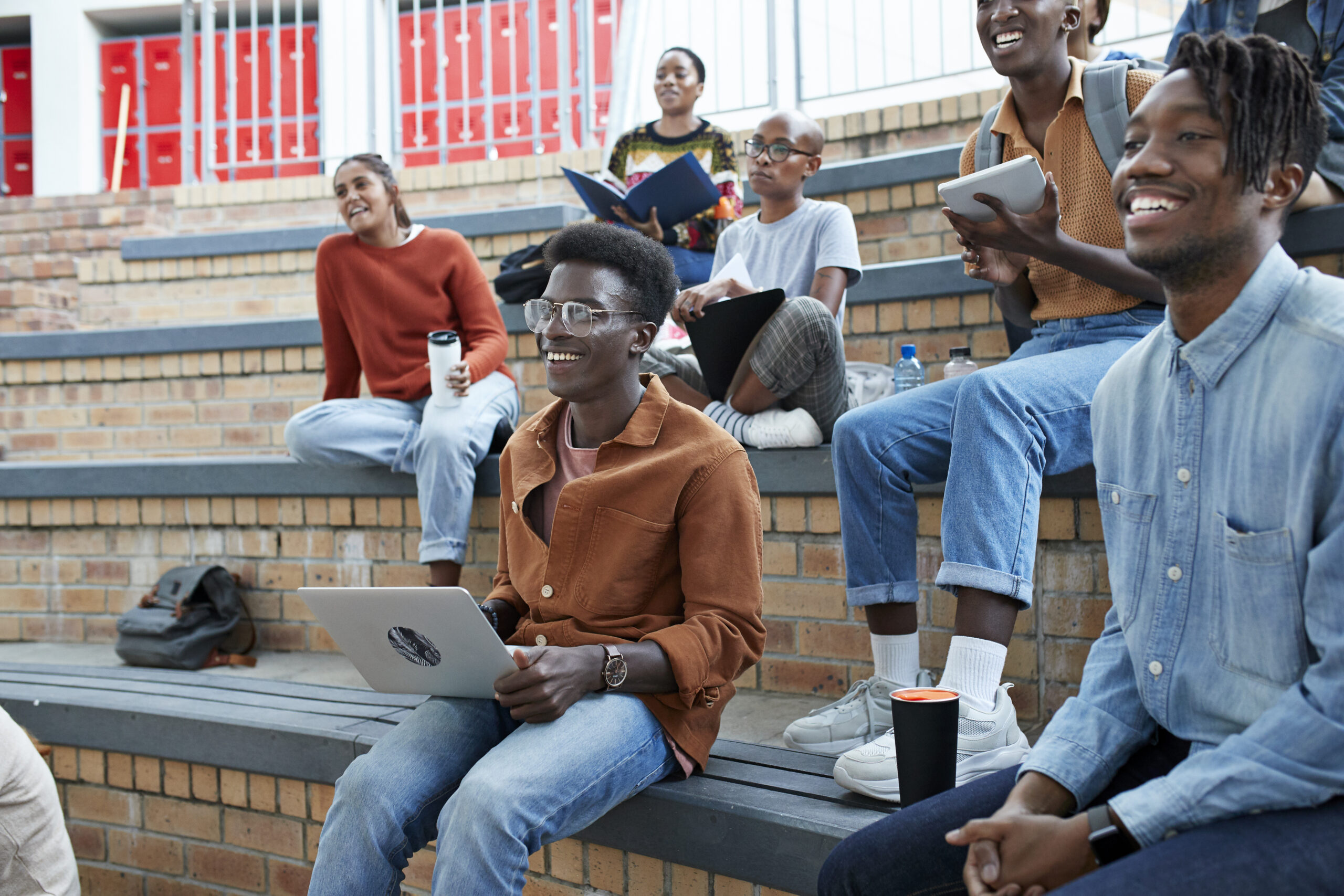 Smiling young multi-ethnic students enjoying while sitting on amphitheater at university campus