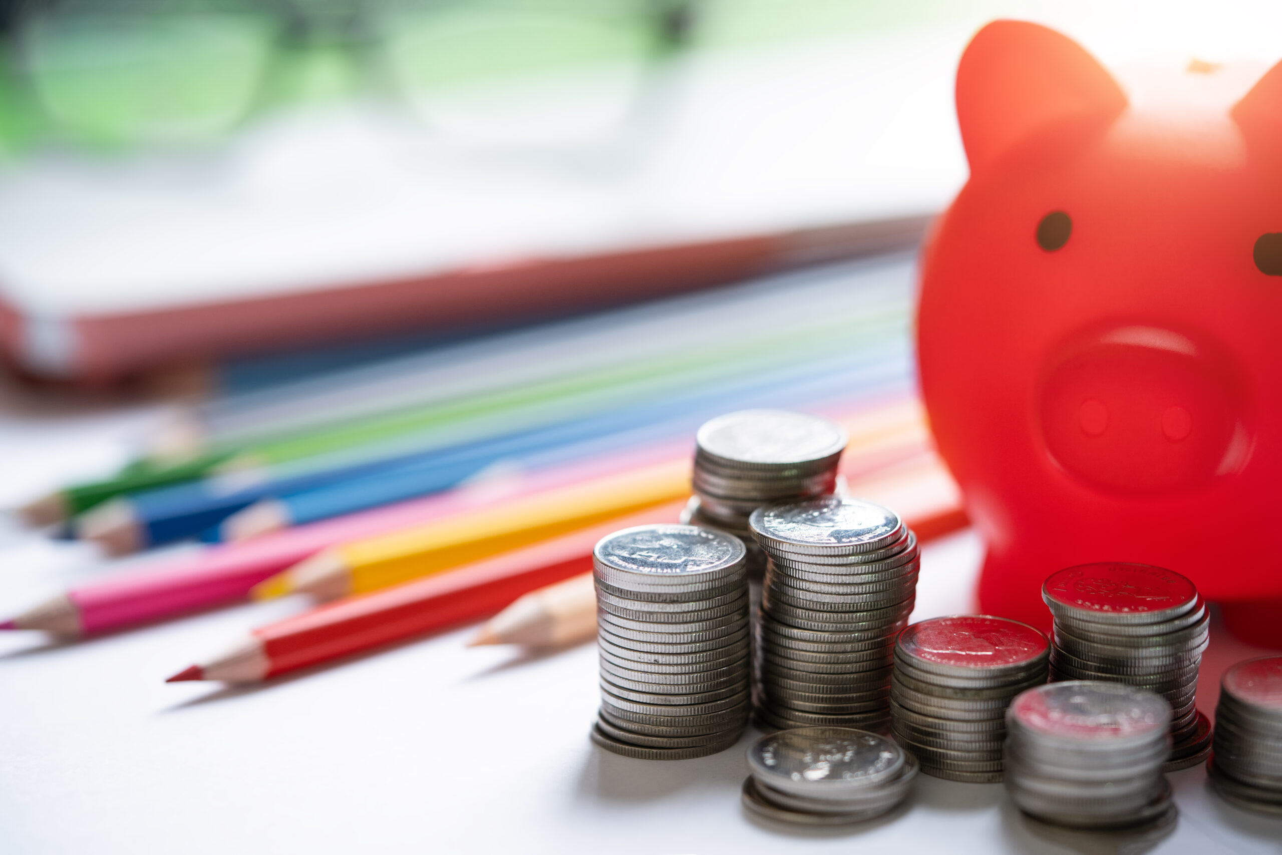 Close up picture of a red piggy bank, some colored pencils and some glasses on top of a desk