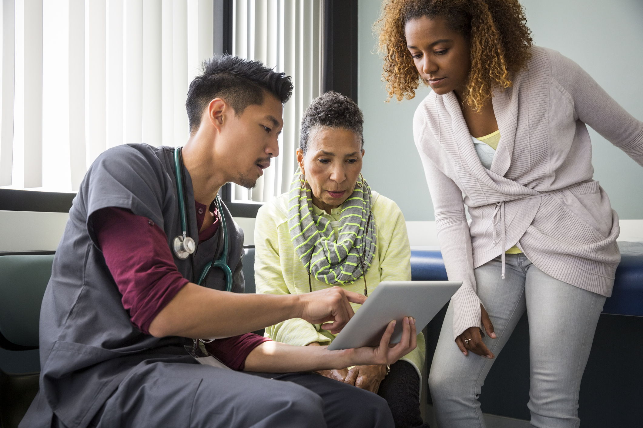 Male nurse consulting with senior female patient and adult daughter in exam room