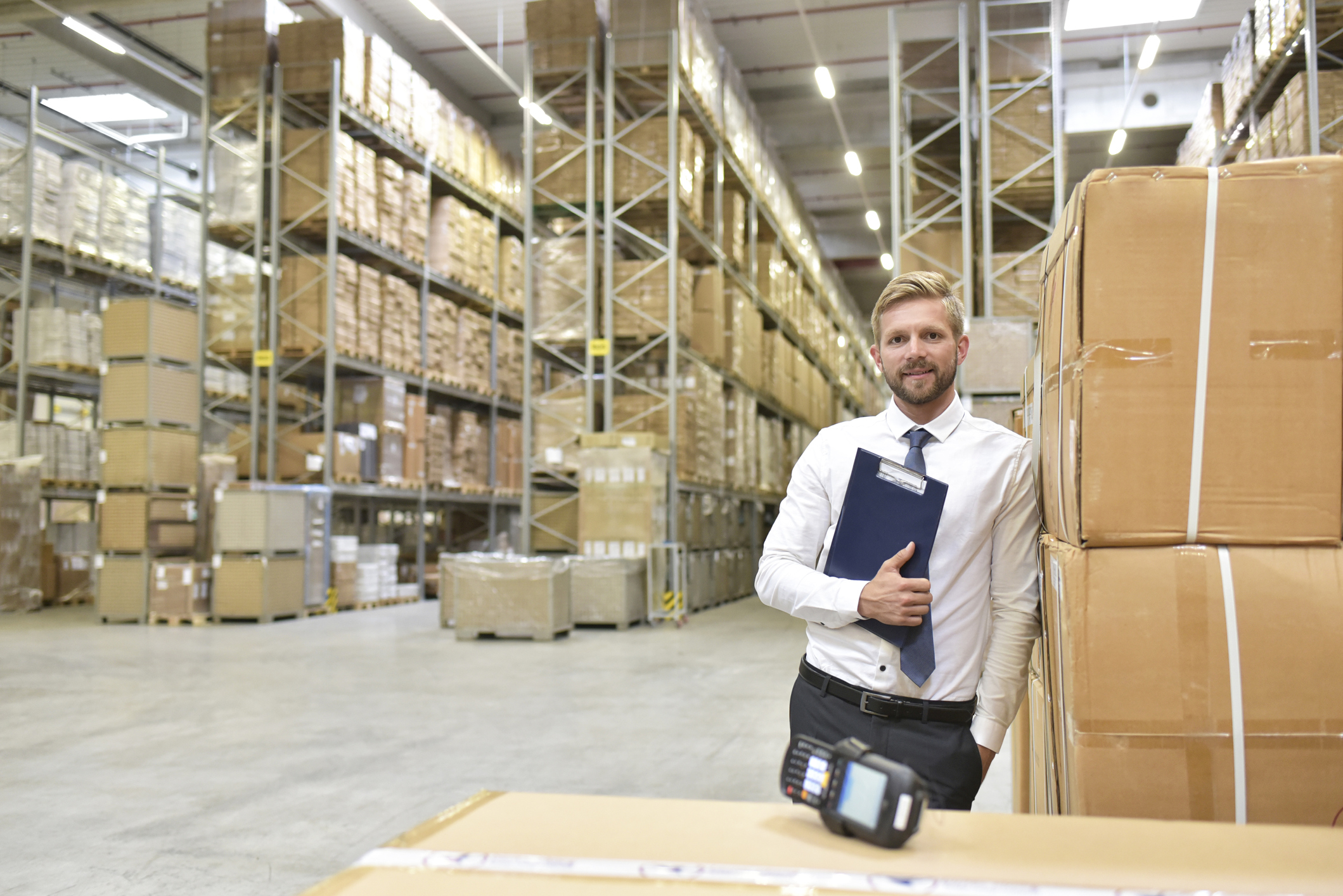 Confident businessman with clipboard and barcode scanner in warehouse