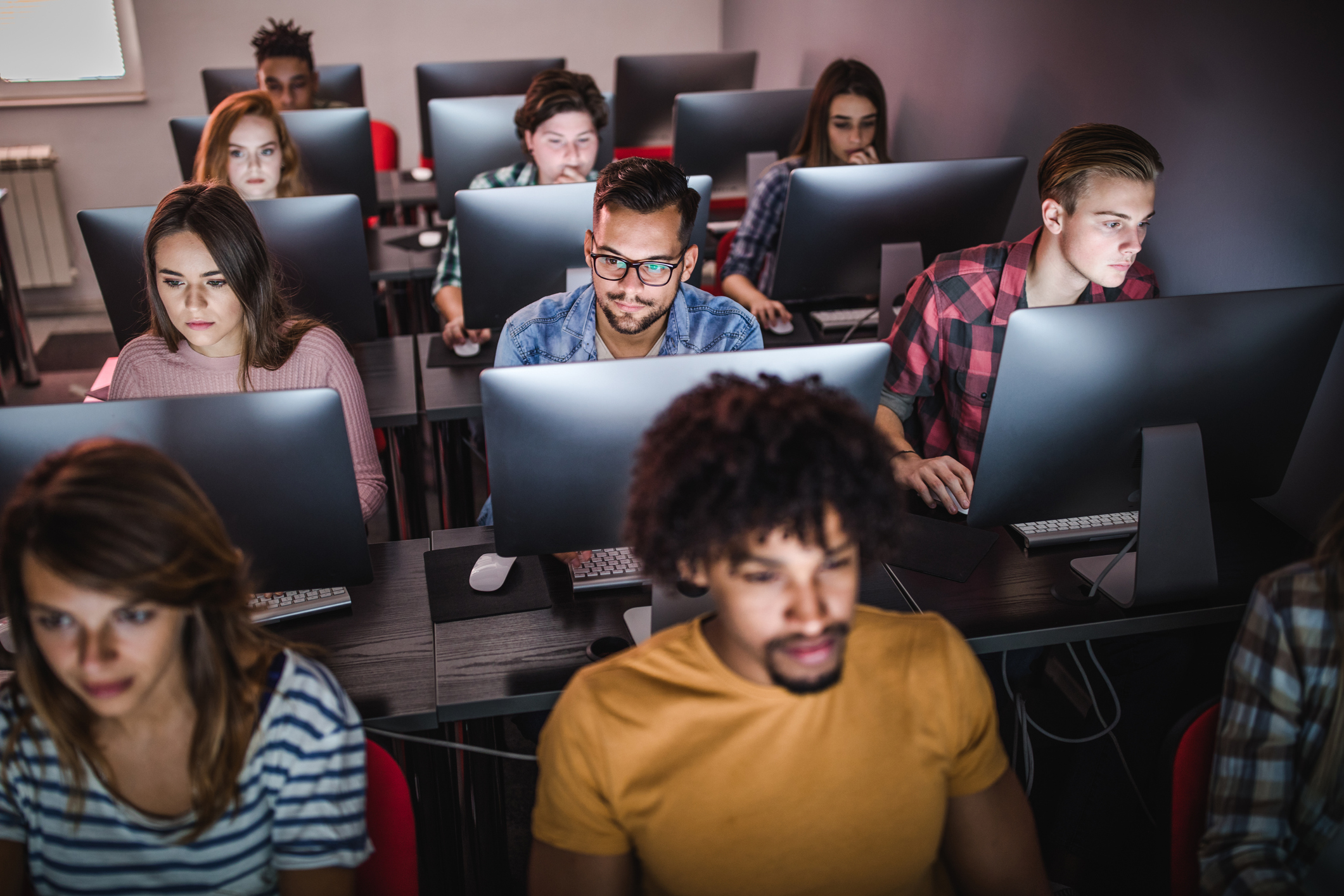 Large group of high school students in a classroom use desktop computers to take a standardized test.