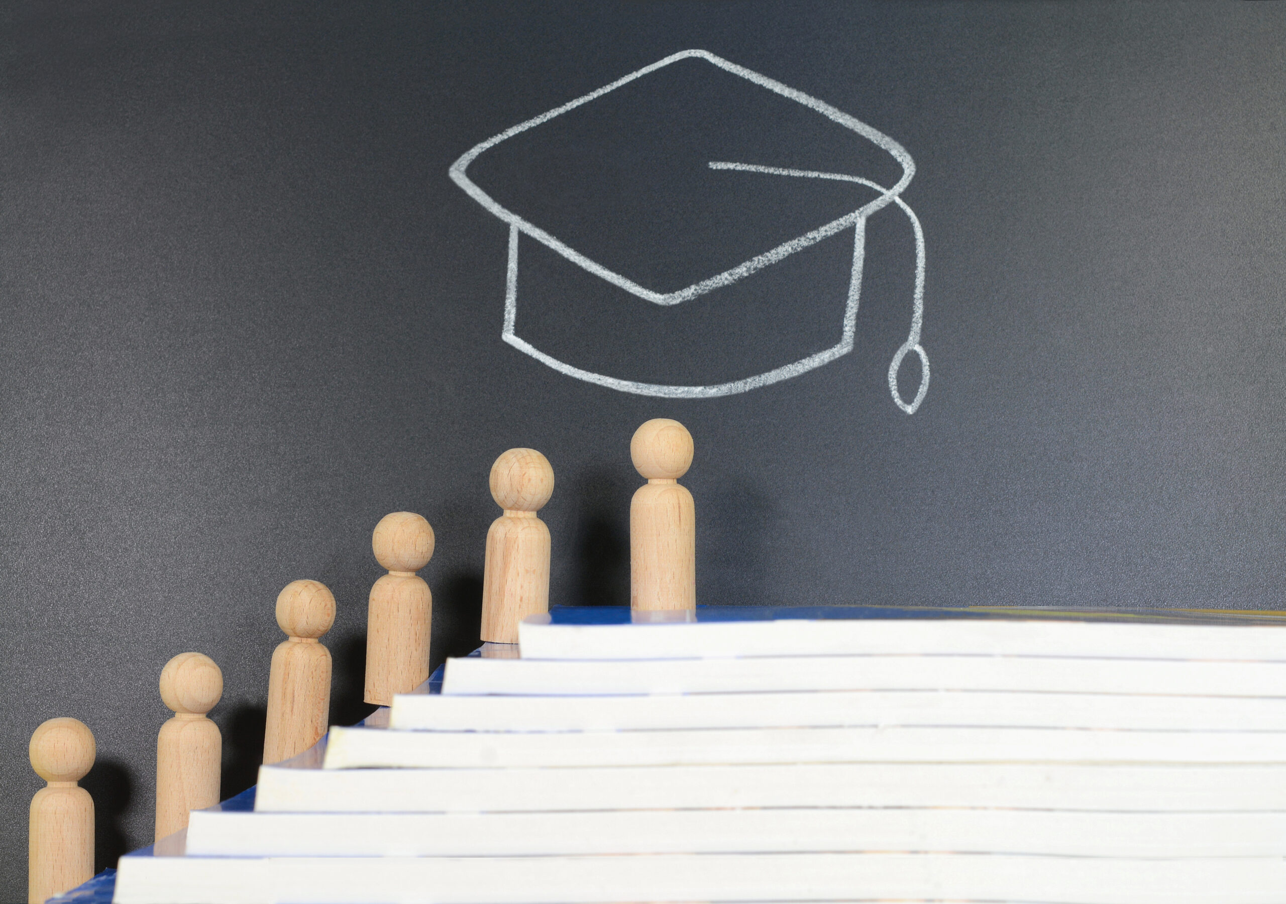 Concept of Graduation. Wooden figurine climbing on top of stacked books with graduation hat drawing on the background.