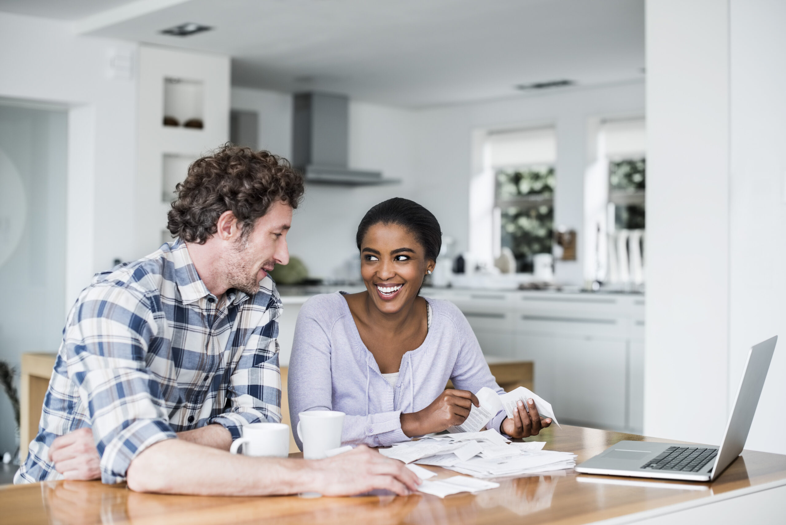 Happy multi-ethnic couple paying bills on laptop at home