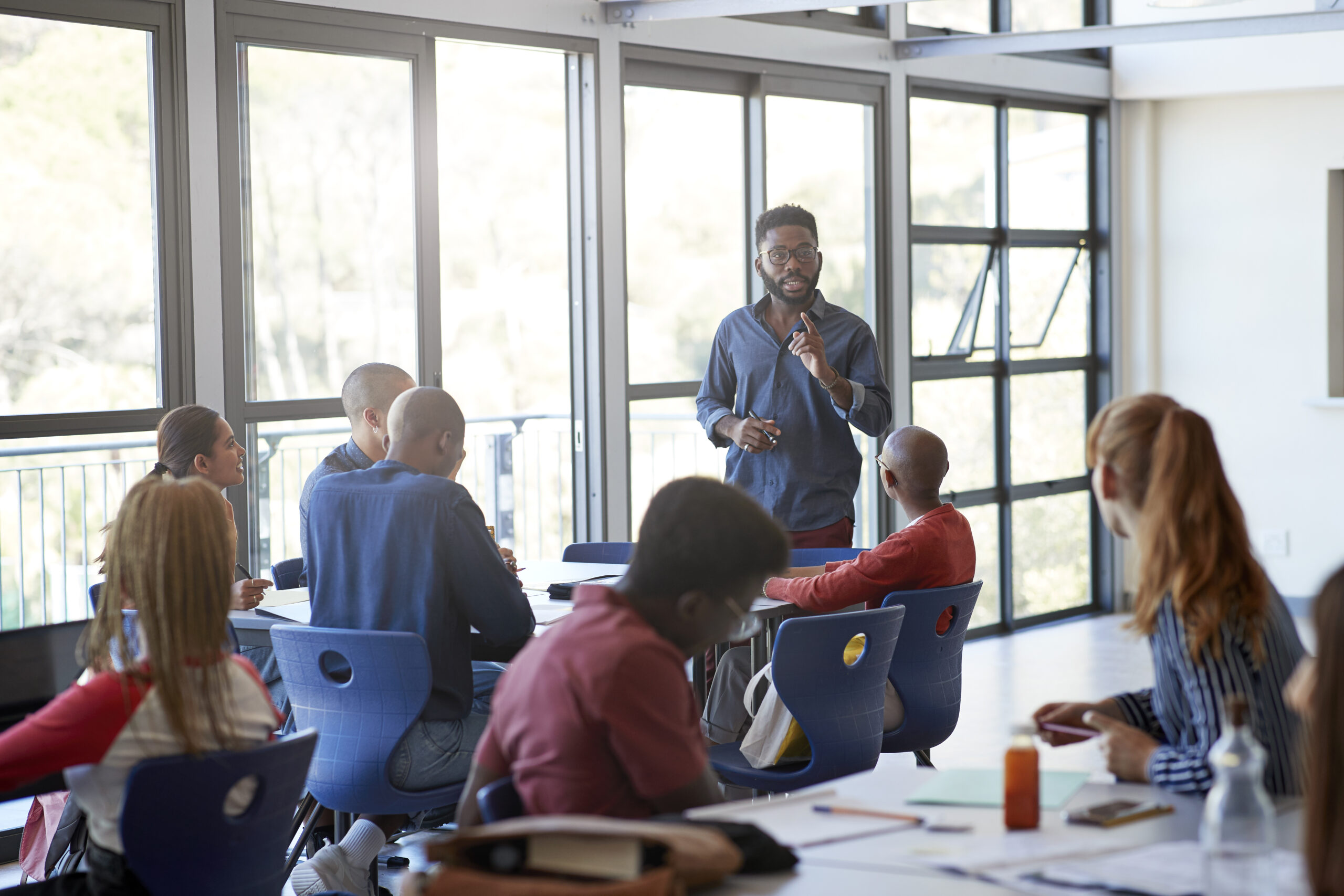 Confident young male professor speaking to multi-ethnic students in community college classroom