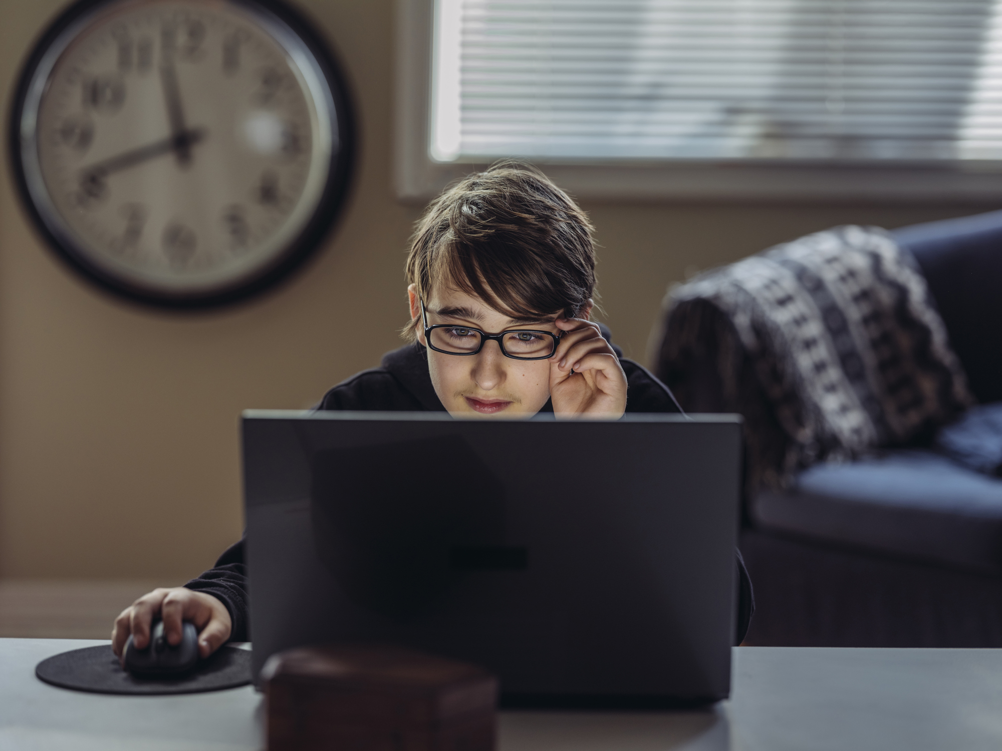 College student with glasses looking at his laptop screen while sitting in his living room.