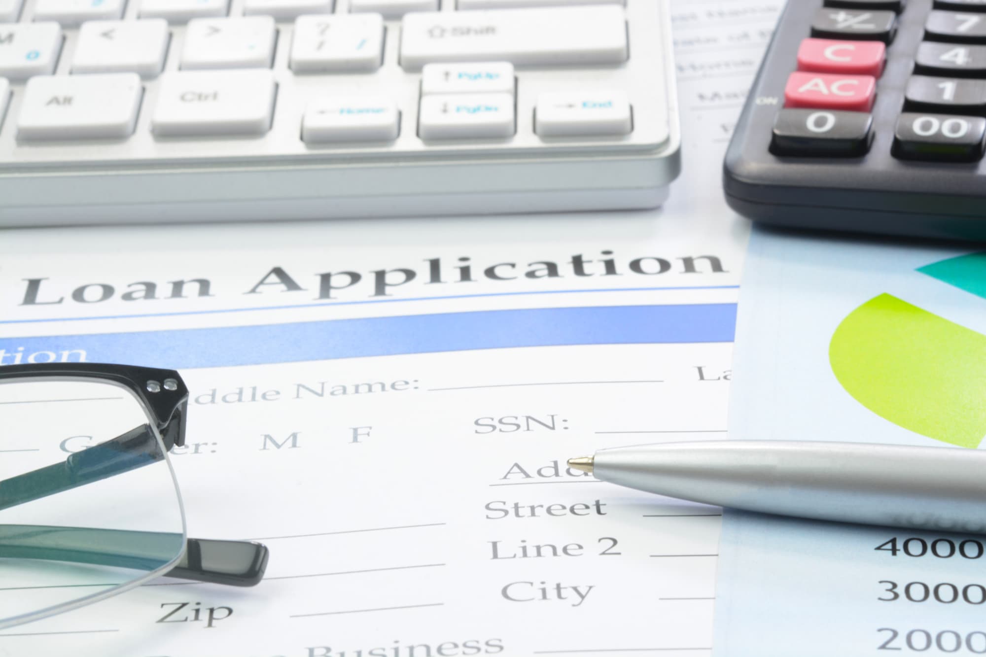 Loan application paperwork on a college student's desk. A pen and calculator are also on the desk next to the loan papers.