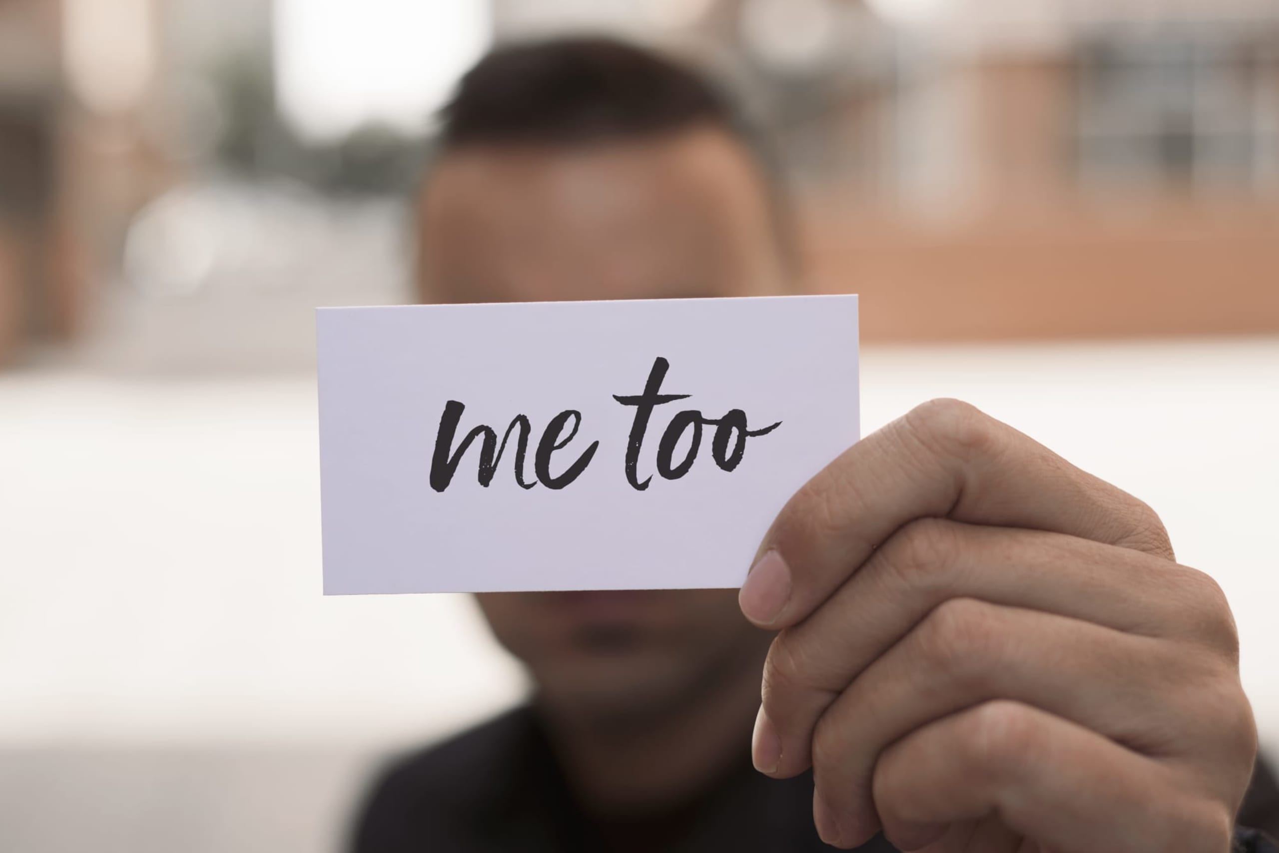 closeup of a young caucasian man in the street showing a piece of paper with the text 'me too' written on it