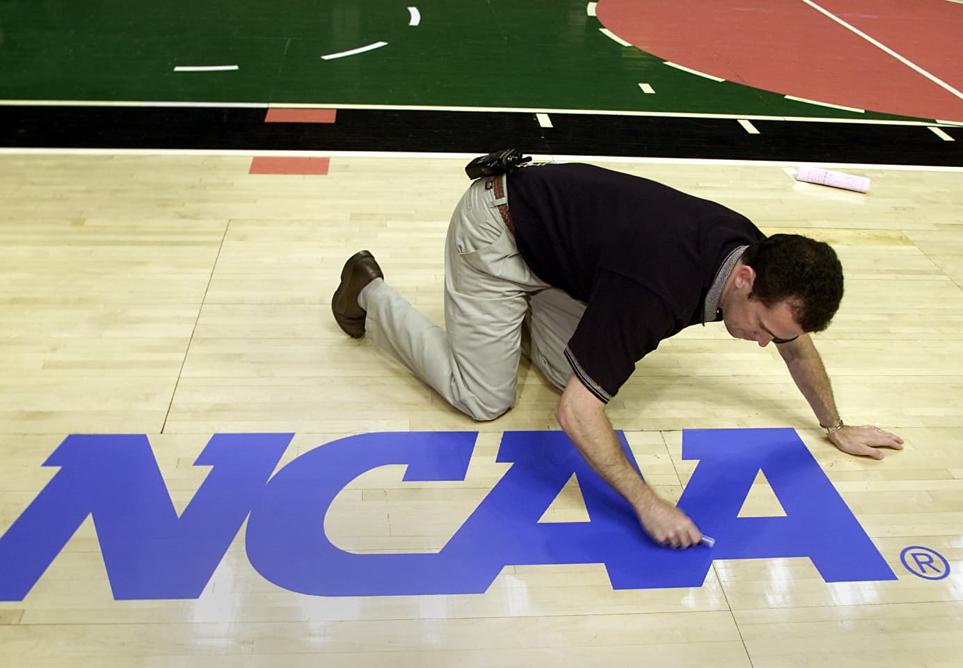 Brent Mater, operations manager for the Arrowhead Pond applies an NCAA logo decal to the basketball floor.