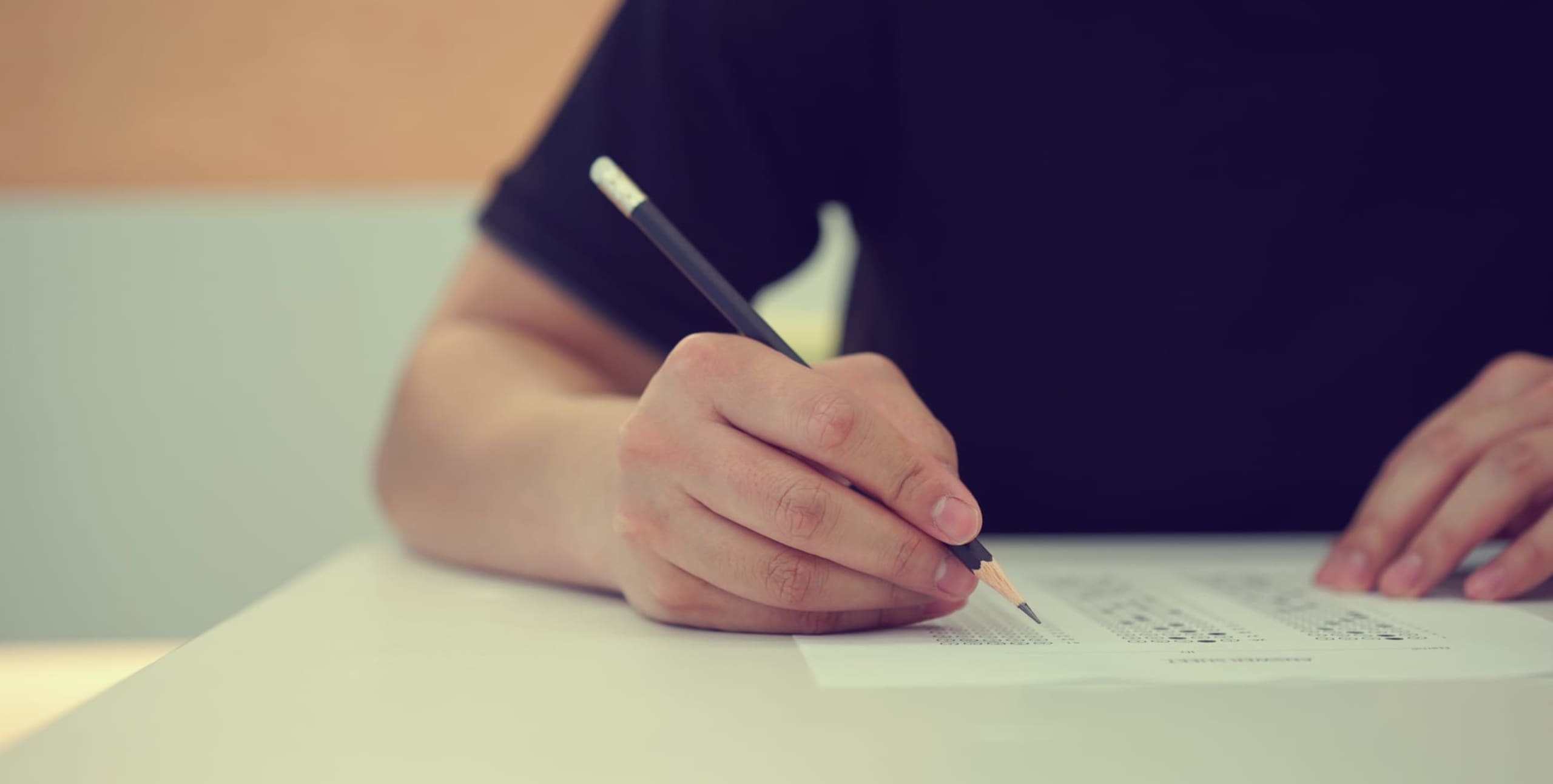 close up high school student man hand writing by marking choices on answer sheet paper for final examination test in classroom concept