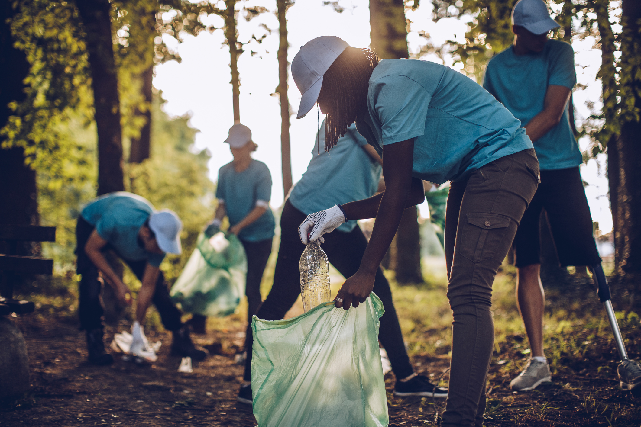 A group of students wearing blue T-shirts pick up trash in an outdoor recreational area.