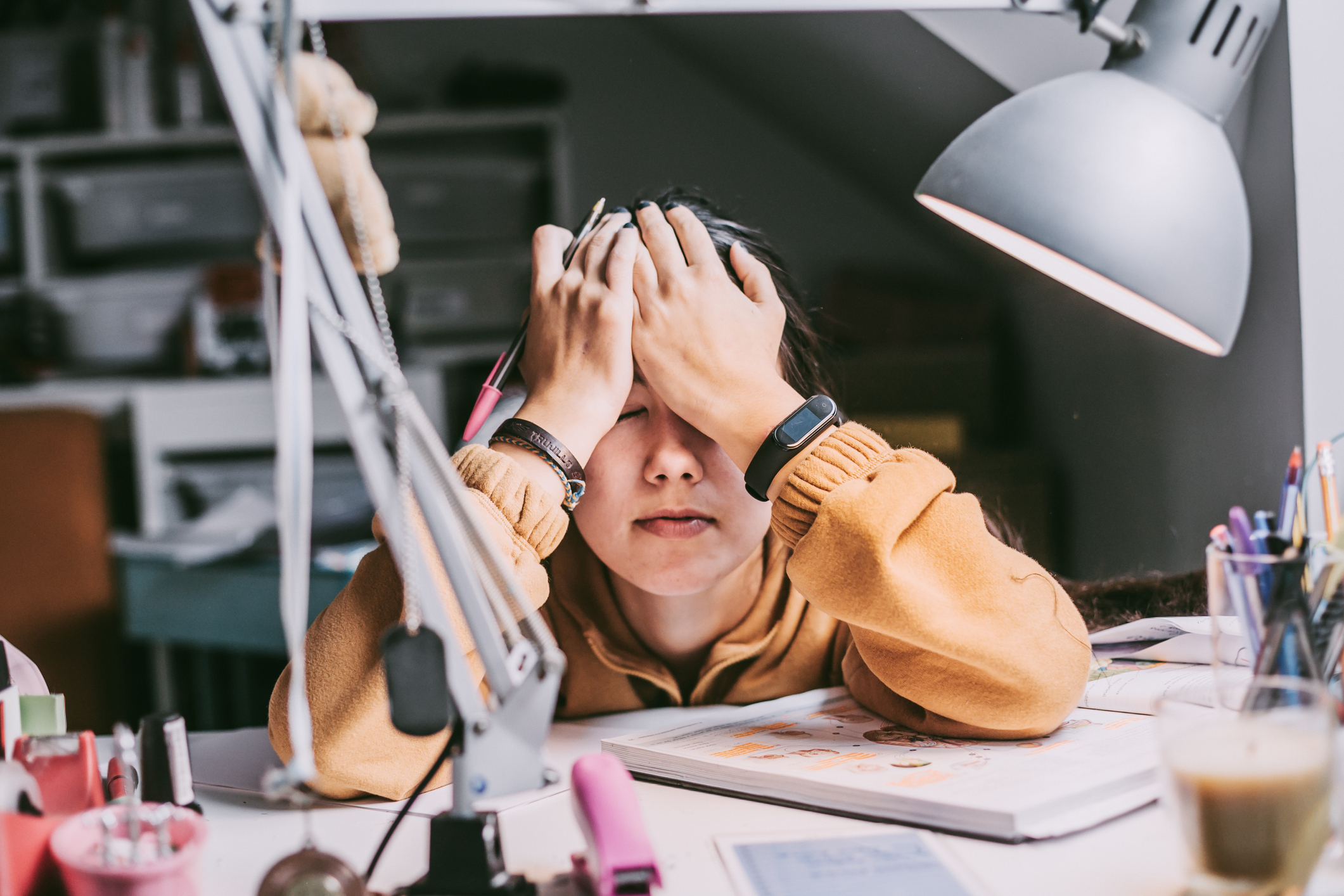 Stressed out high school student sitting at her bedroom desk at home with her head resting against her forehead in a moment of frustration.