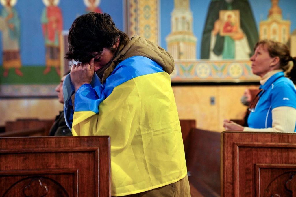 A man dressed in the blue and yellow of Ukraine's flag weeps and kneels as Ukrainian families gather for mass at Saints Volodymyr and Olha Ukrainian Church in Chicago, IL.