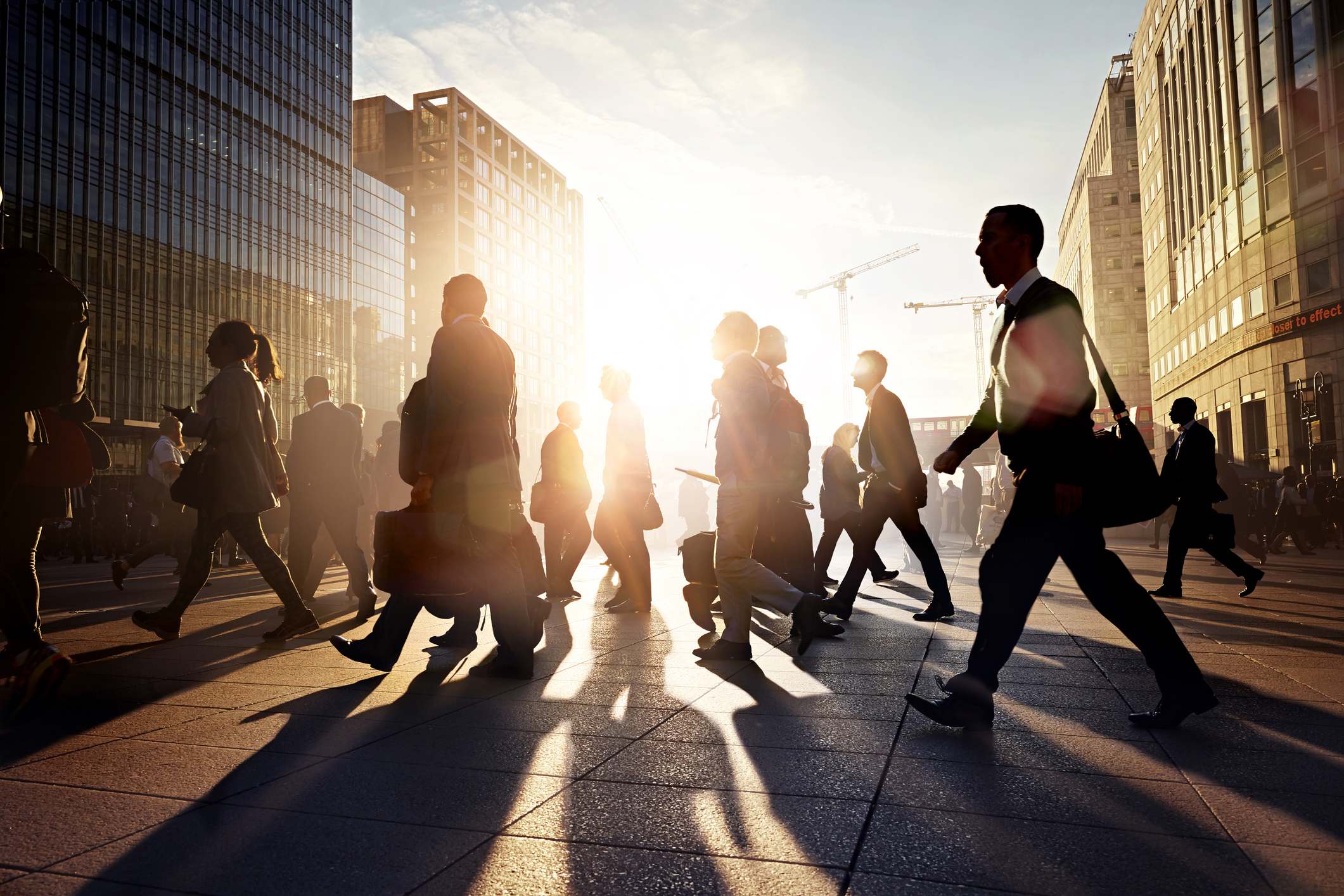 People crossing a city square on their way to work on a sunny morning.