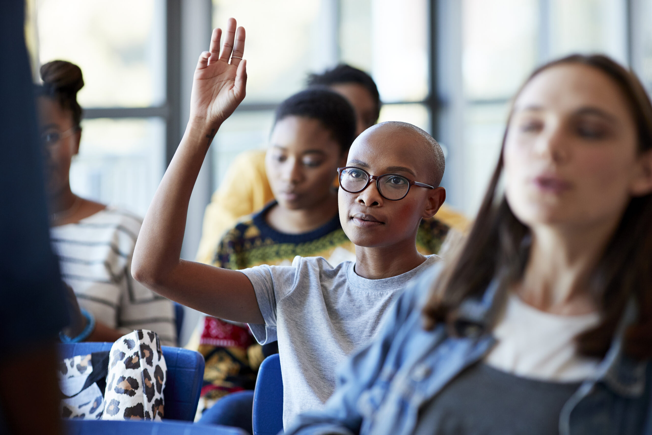 Confident young student sitting with arms raised around friends in classroom at community college