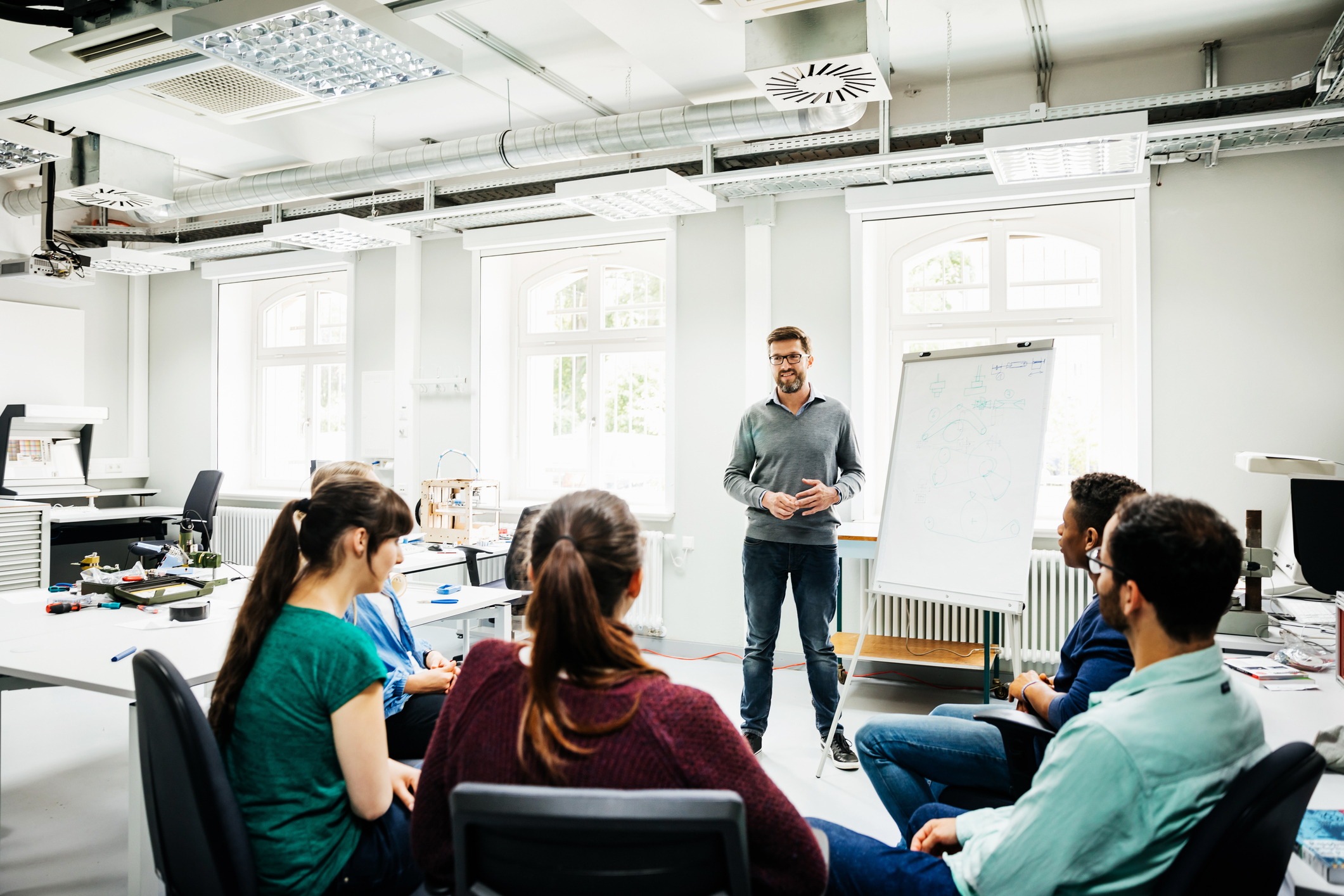 An engineering tutor speaking to his students during a seminar in a bright, modern lab at a university.