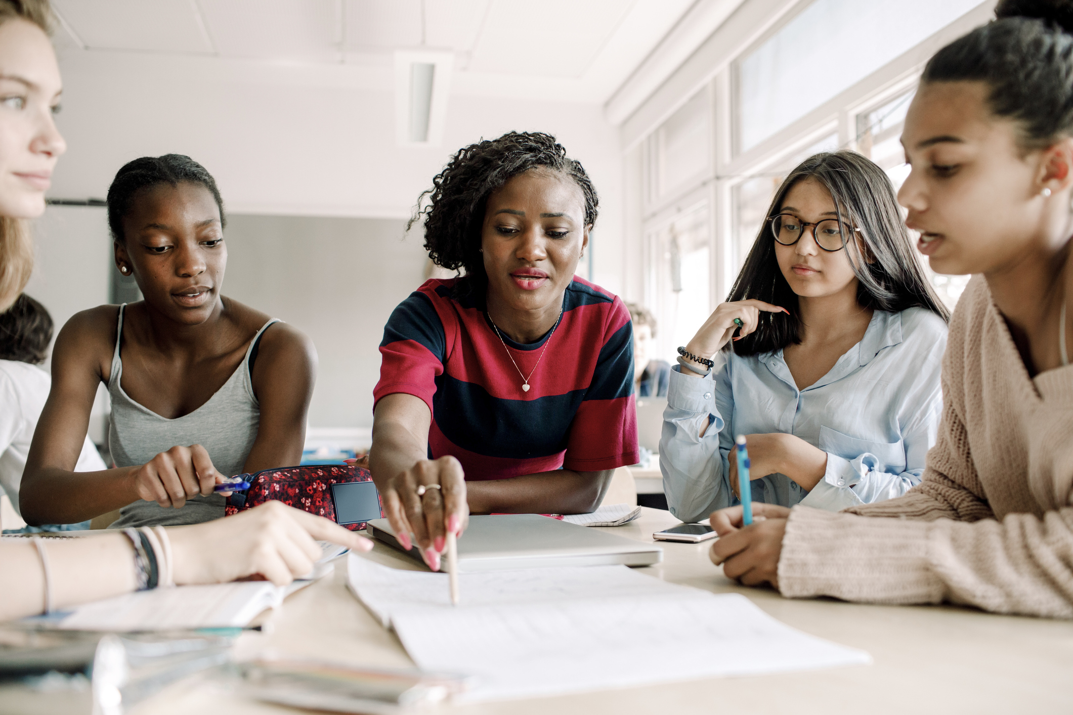 Teacher explaining while female students studying by table in classroom