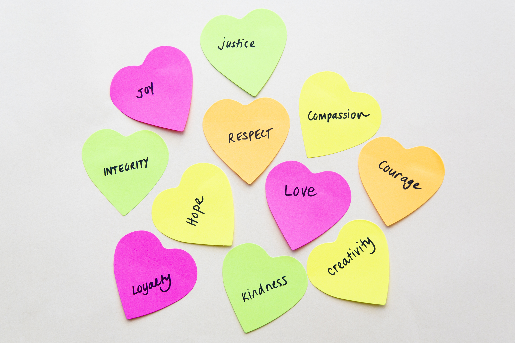 Values such as courage, justice, and creativity handwritten on heart shaped sticky notes.