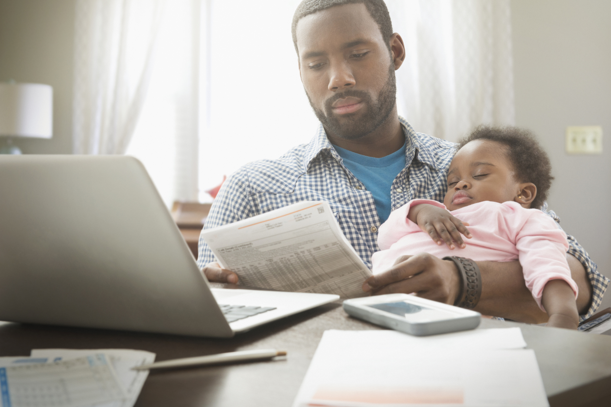 Father holding his baby daughter while trying to work from home.