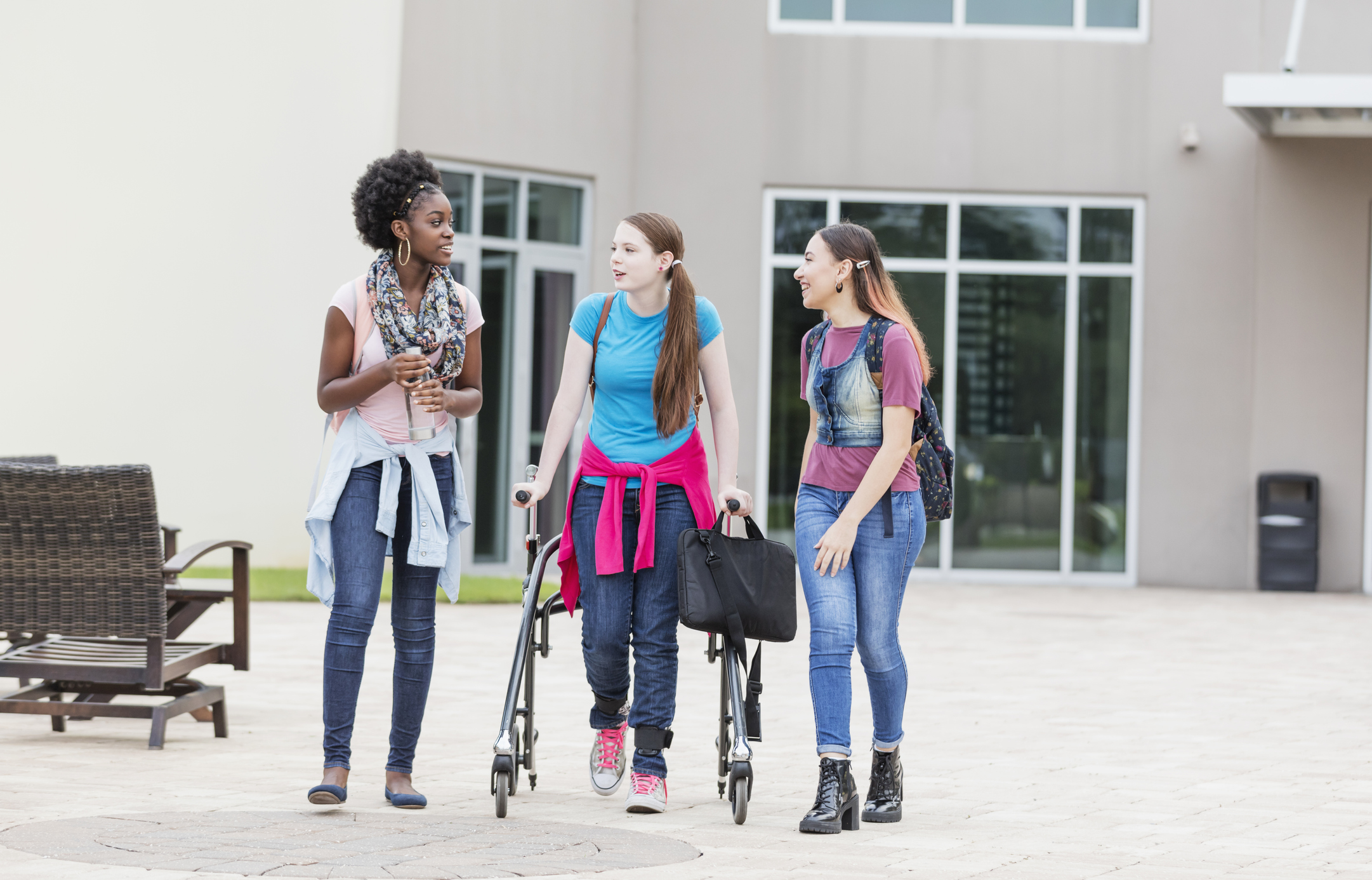 Disabled student using a walker chats with her friends while walking to class on a college campus.