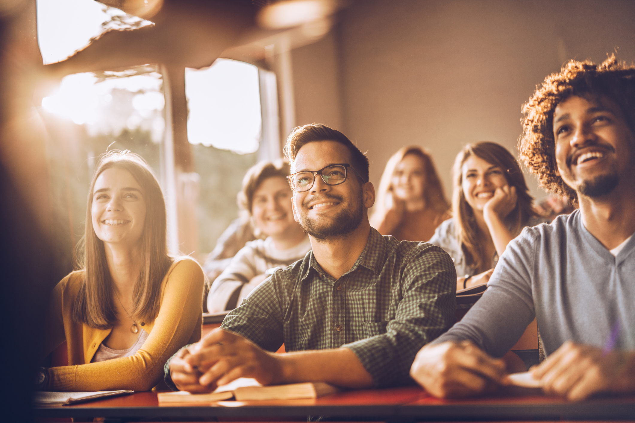 Group of happy students listening to a professor speaking during class.