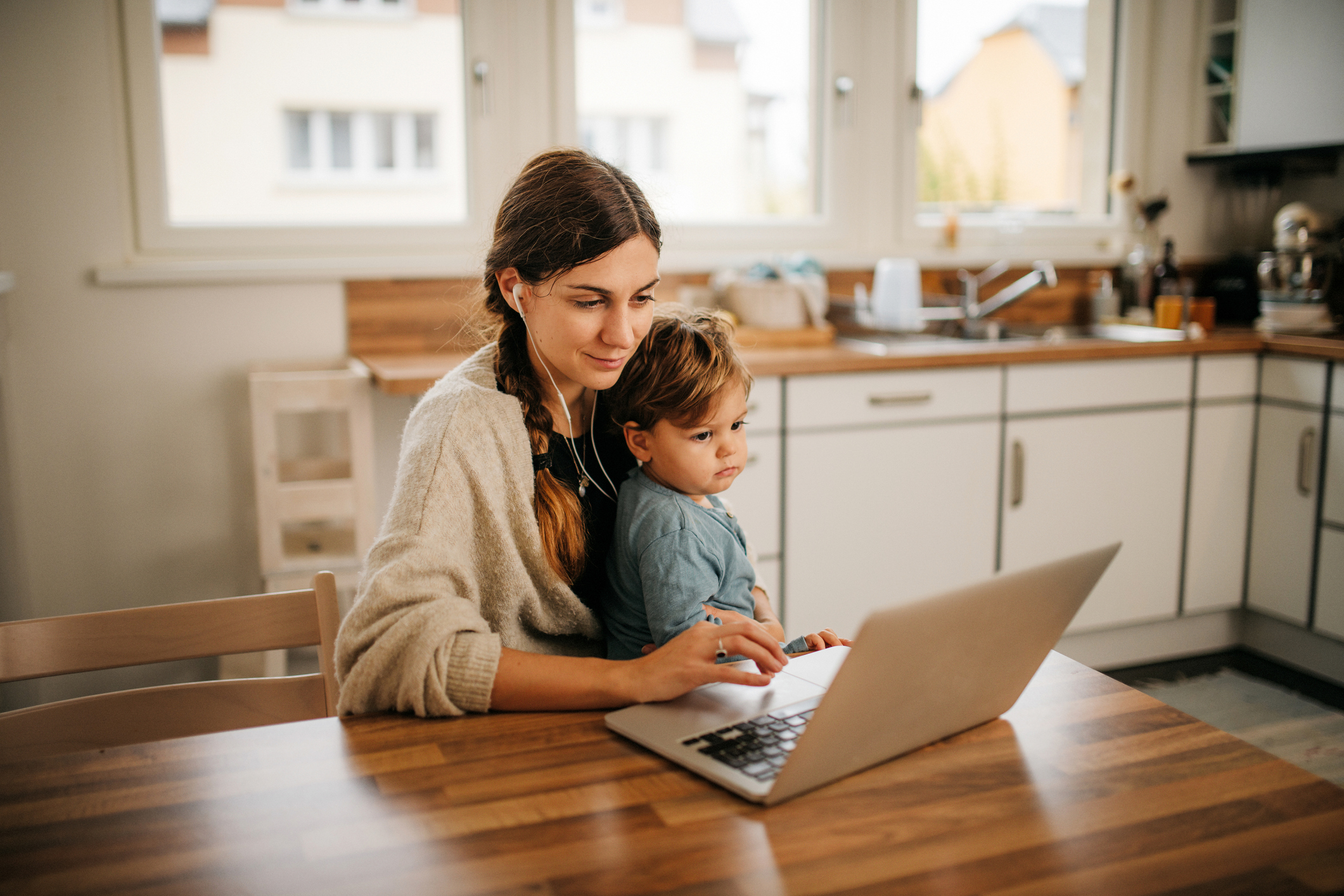 College student sitting at home with her young child listening to a class lecture on her laptop.