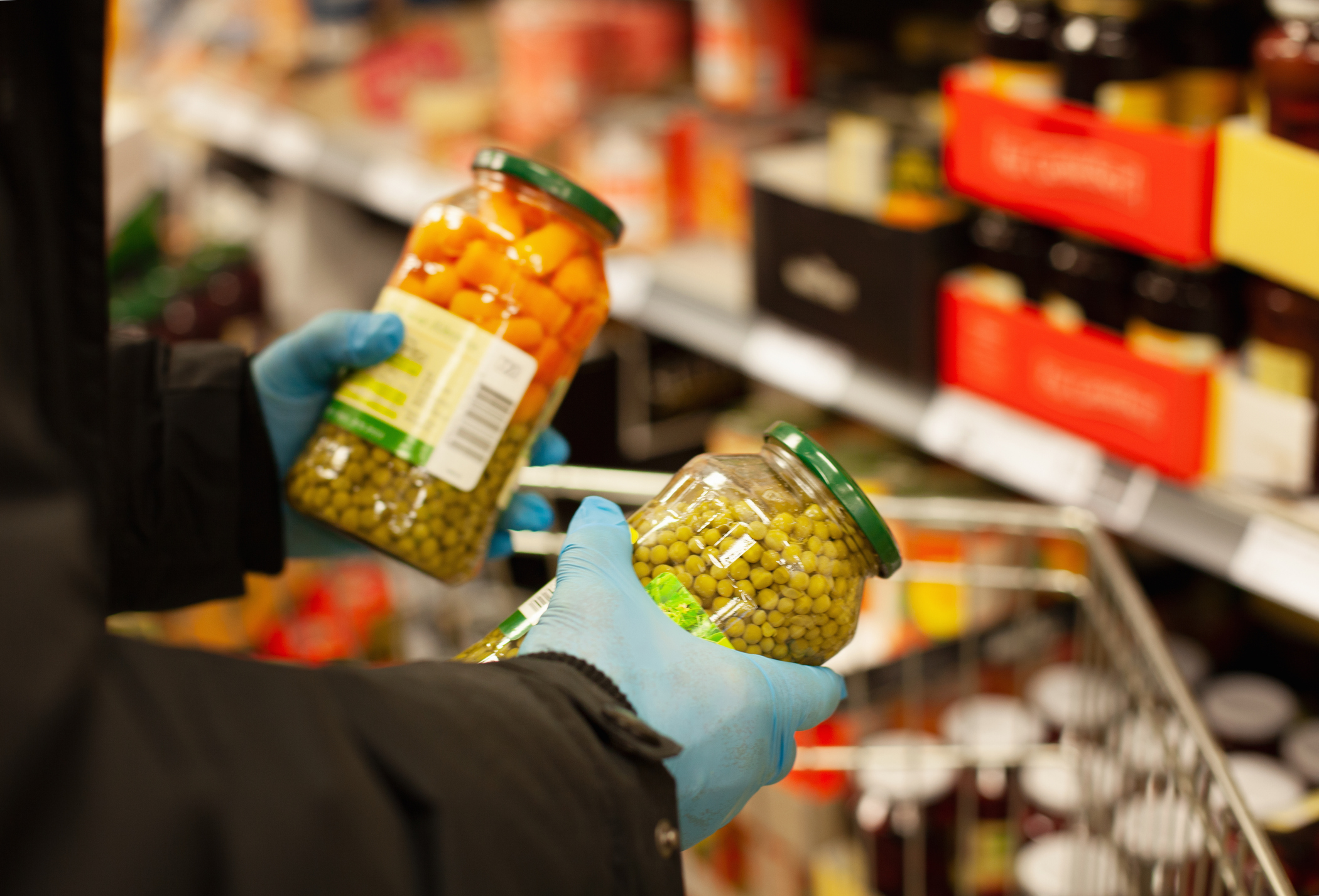 Man shopping for preserved vegetables at supermarket, wearing protective gloves