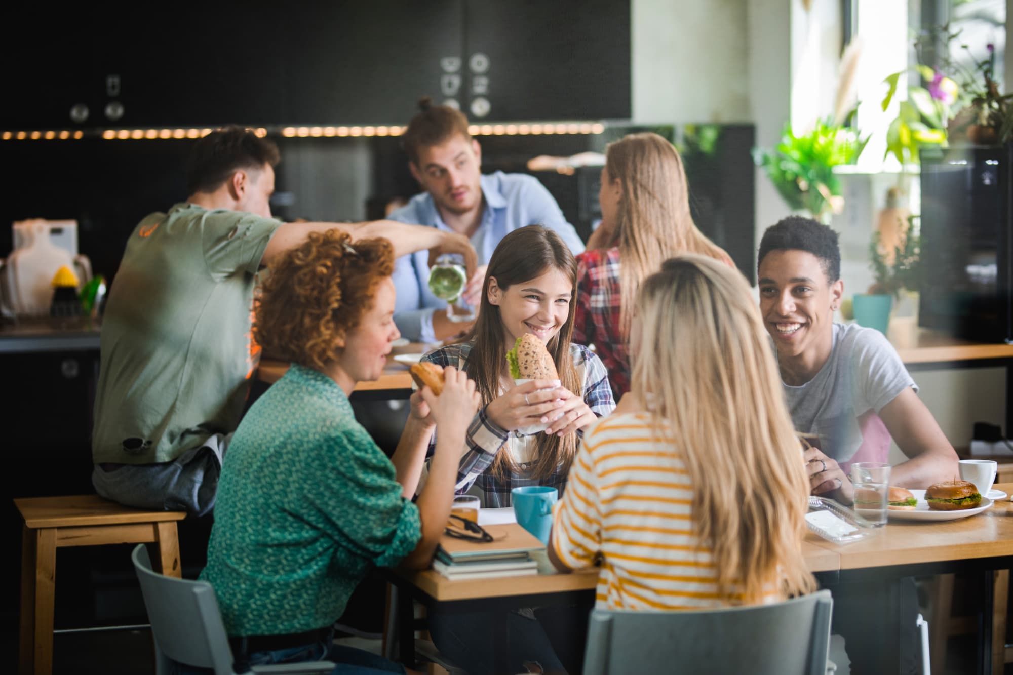 A group of college students chatting while eating lunch in a university dining hall.