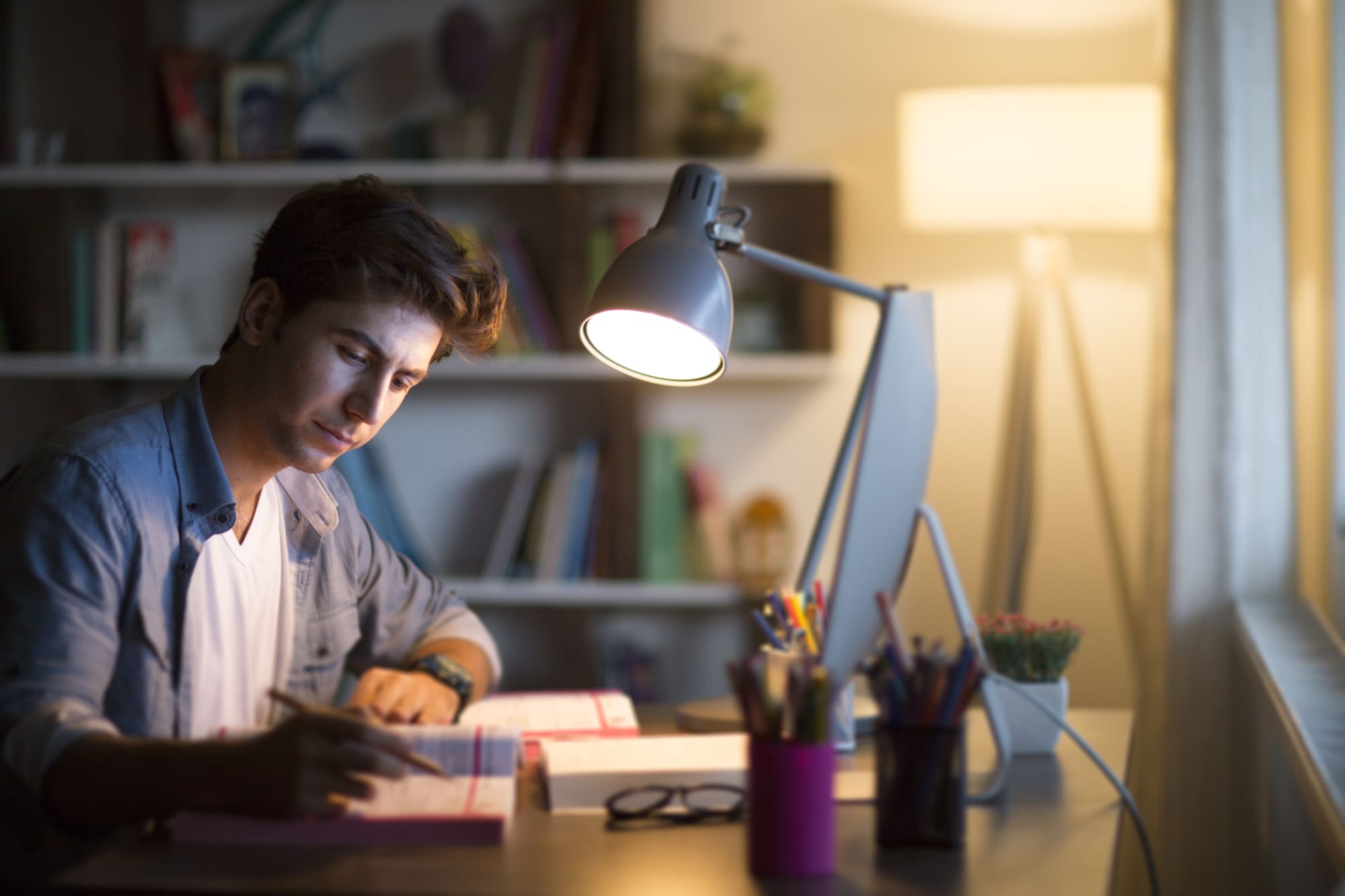 A student is working in a dimly lit space with a computer and a notebook.