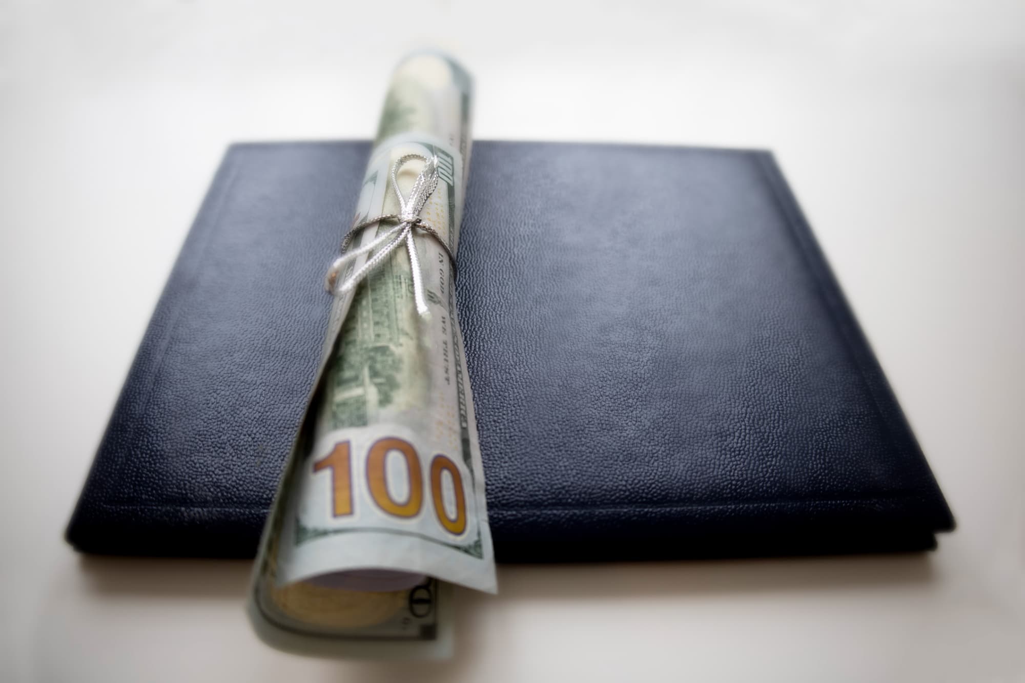 A picture of a $100 bill folded like a diploma, sitting atop a graduation cap