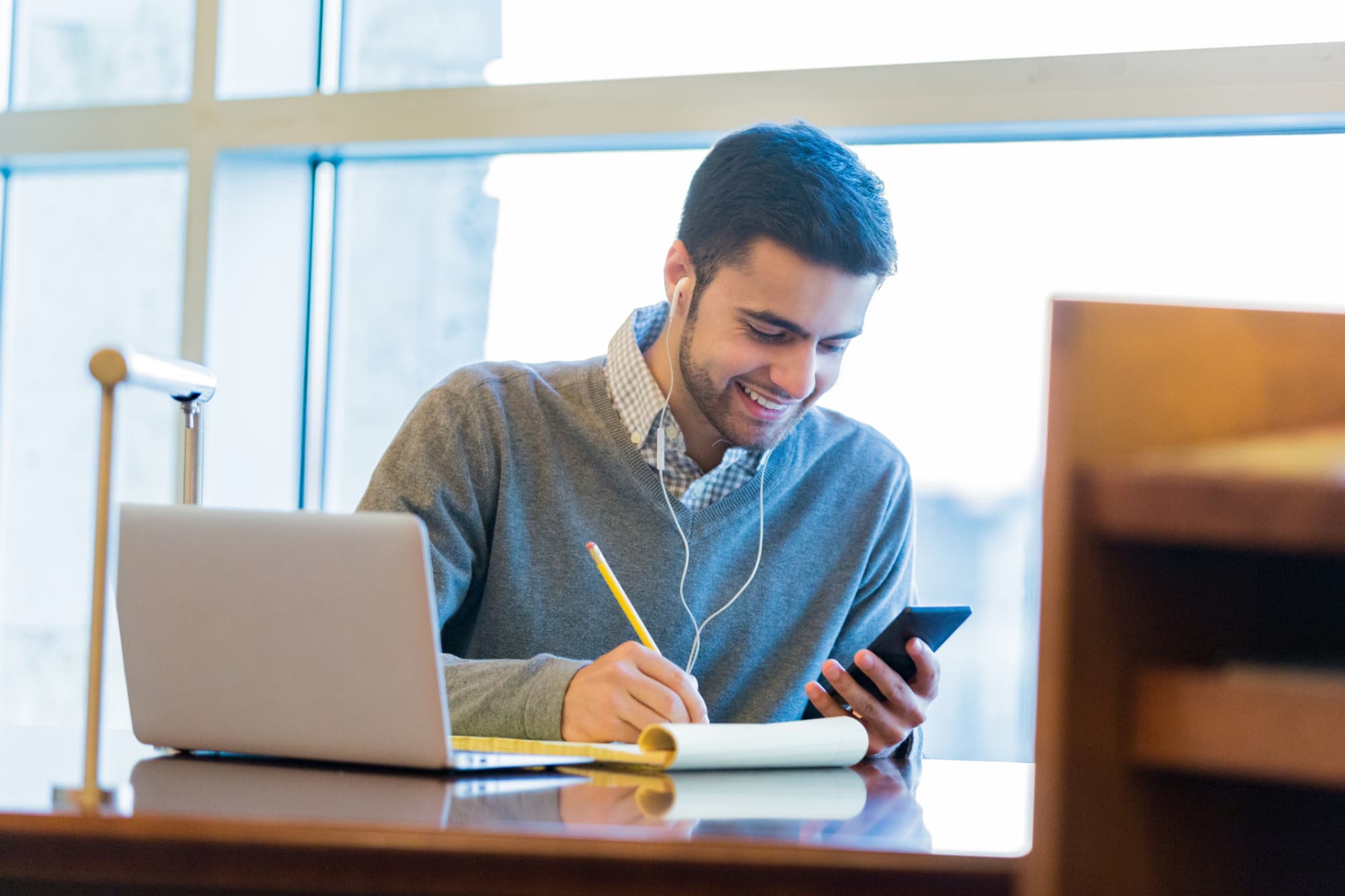 Student checking college application deadlines on his mobile phone while working on college application forms for his laptop.