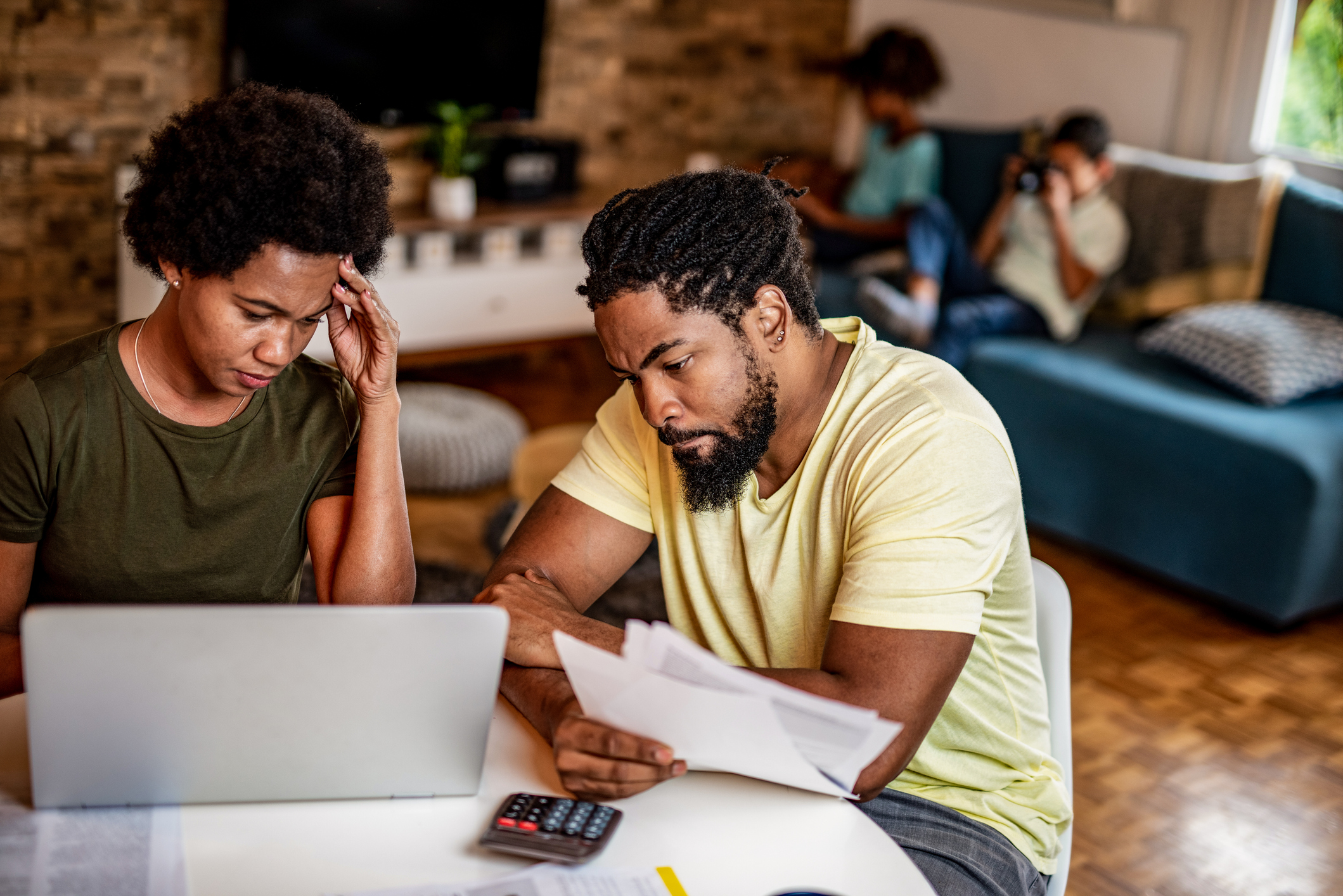 Worries parents doing home finances in the living room. Children sitting in the background.